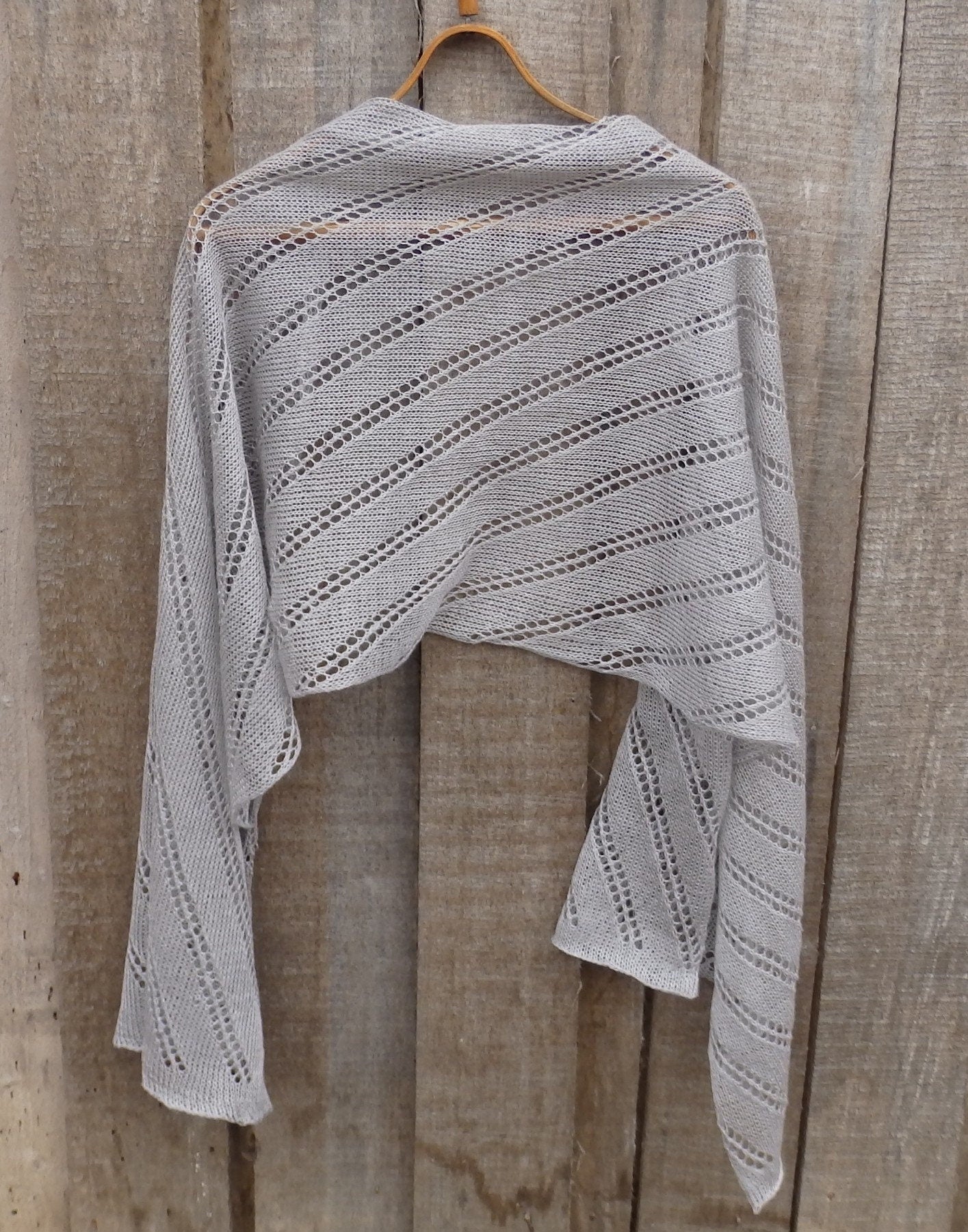 Knitted shawl draped over a wooden hanger against a wooden background