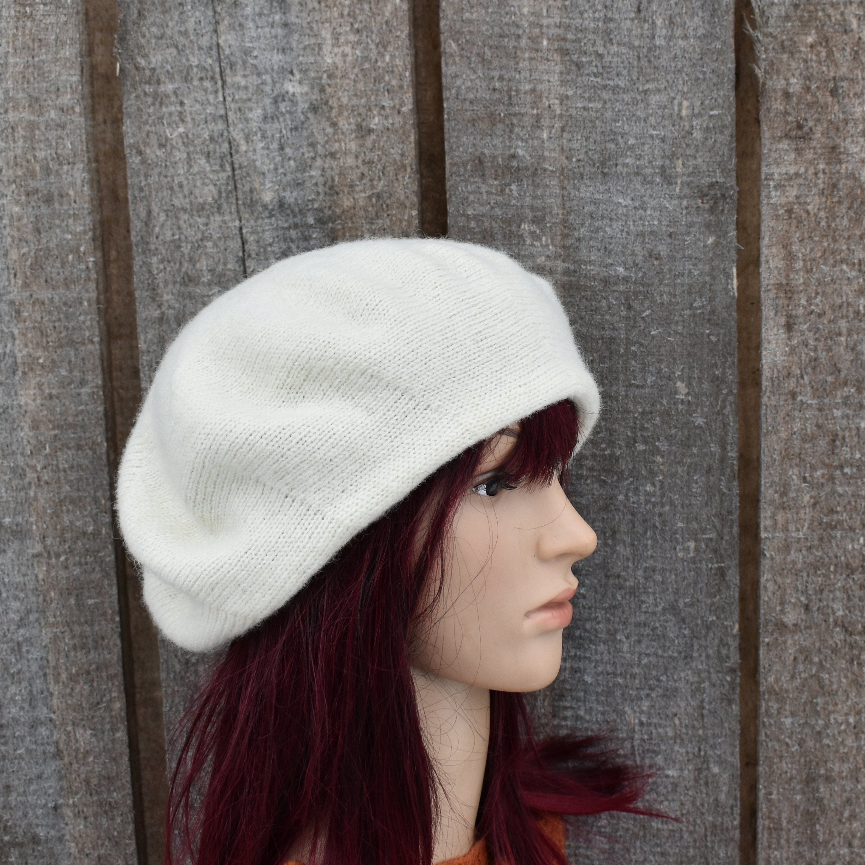 Mannequin head wearing a white knit beret against a wooden background