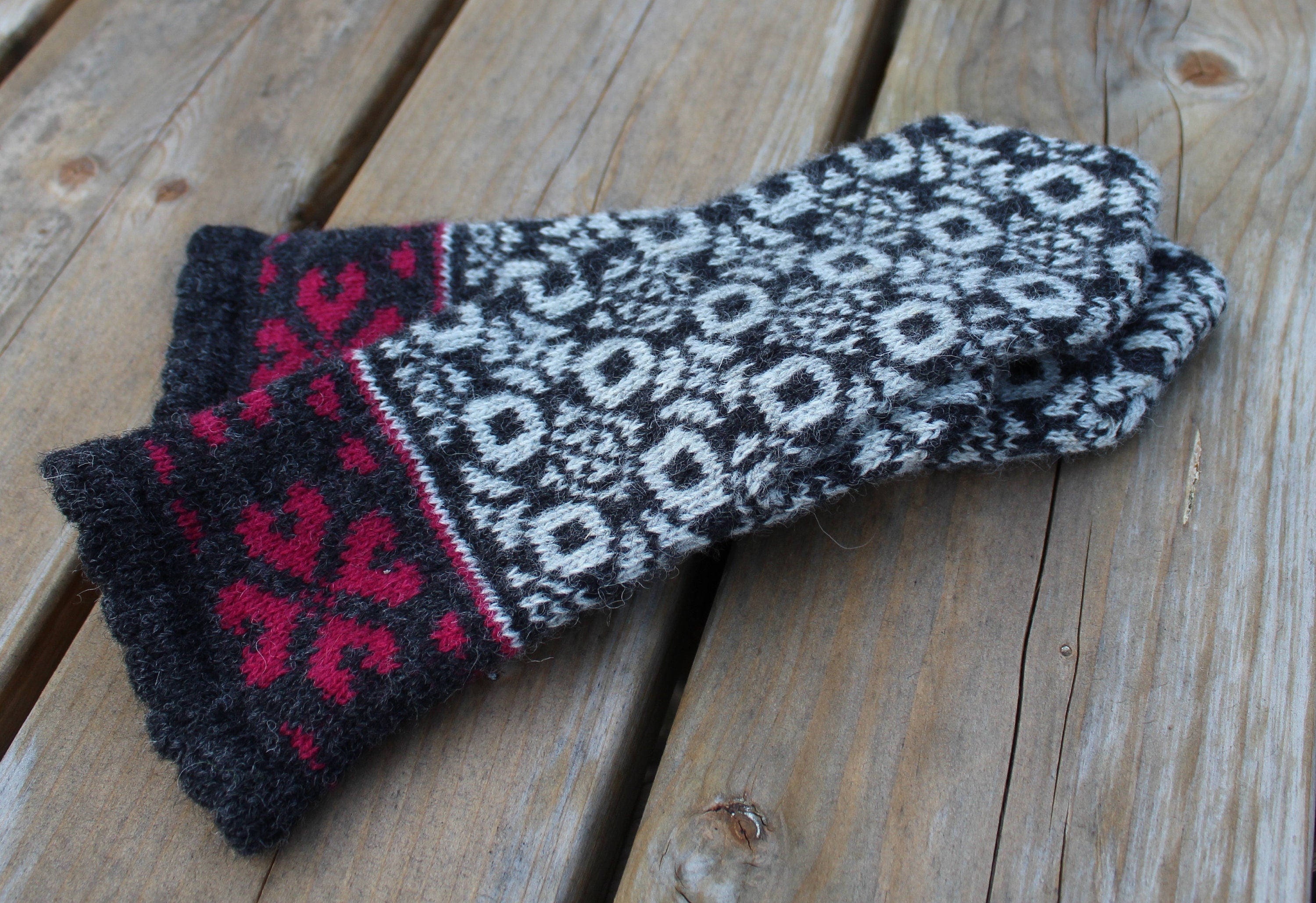 Pair of knitted gloves with a black, white, and red pattern on a wooden surface