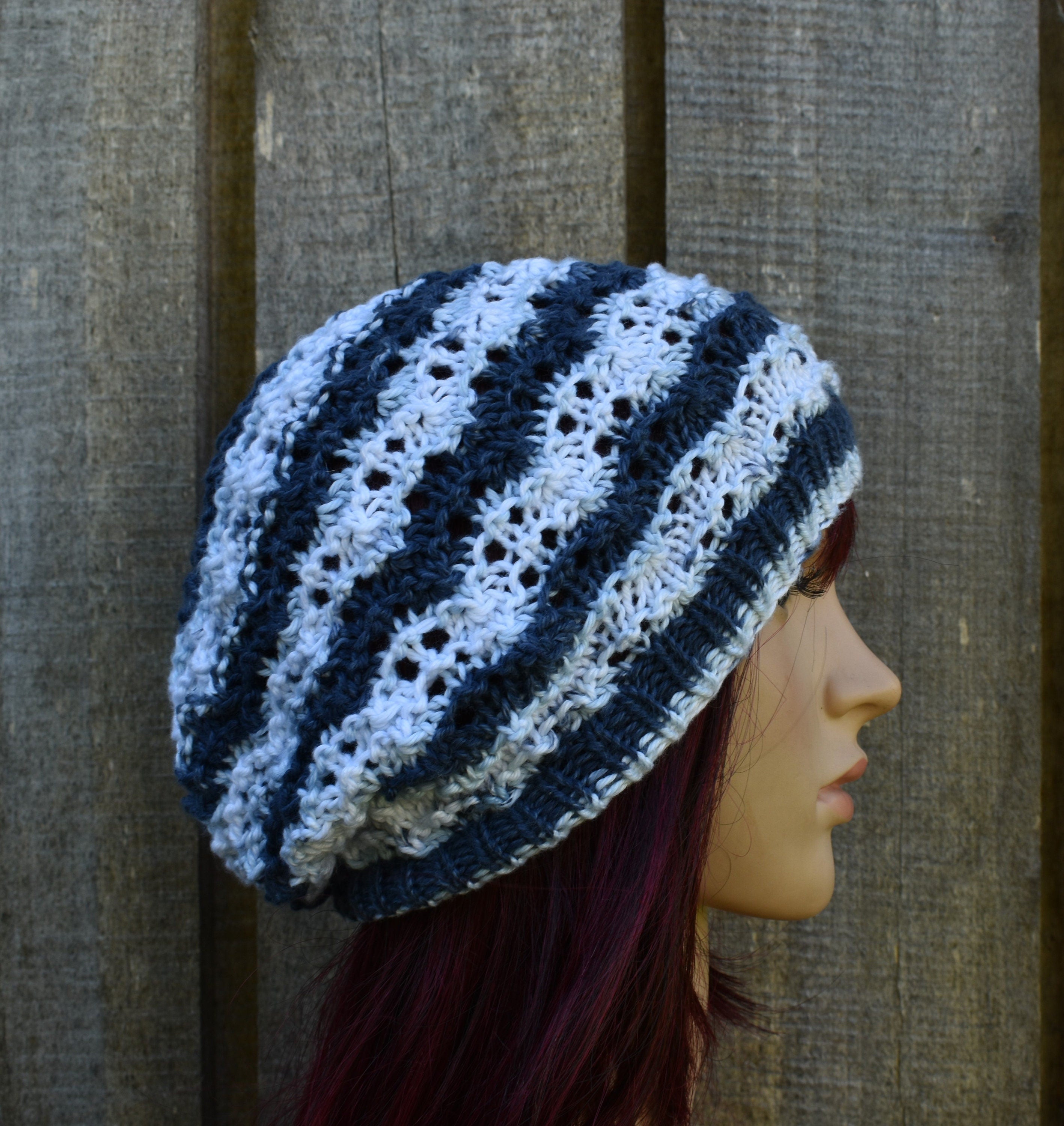 Crocheted beanie with blue and white stripes on a mannequin head against a wooden background