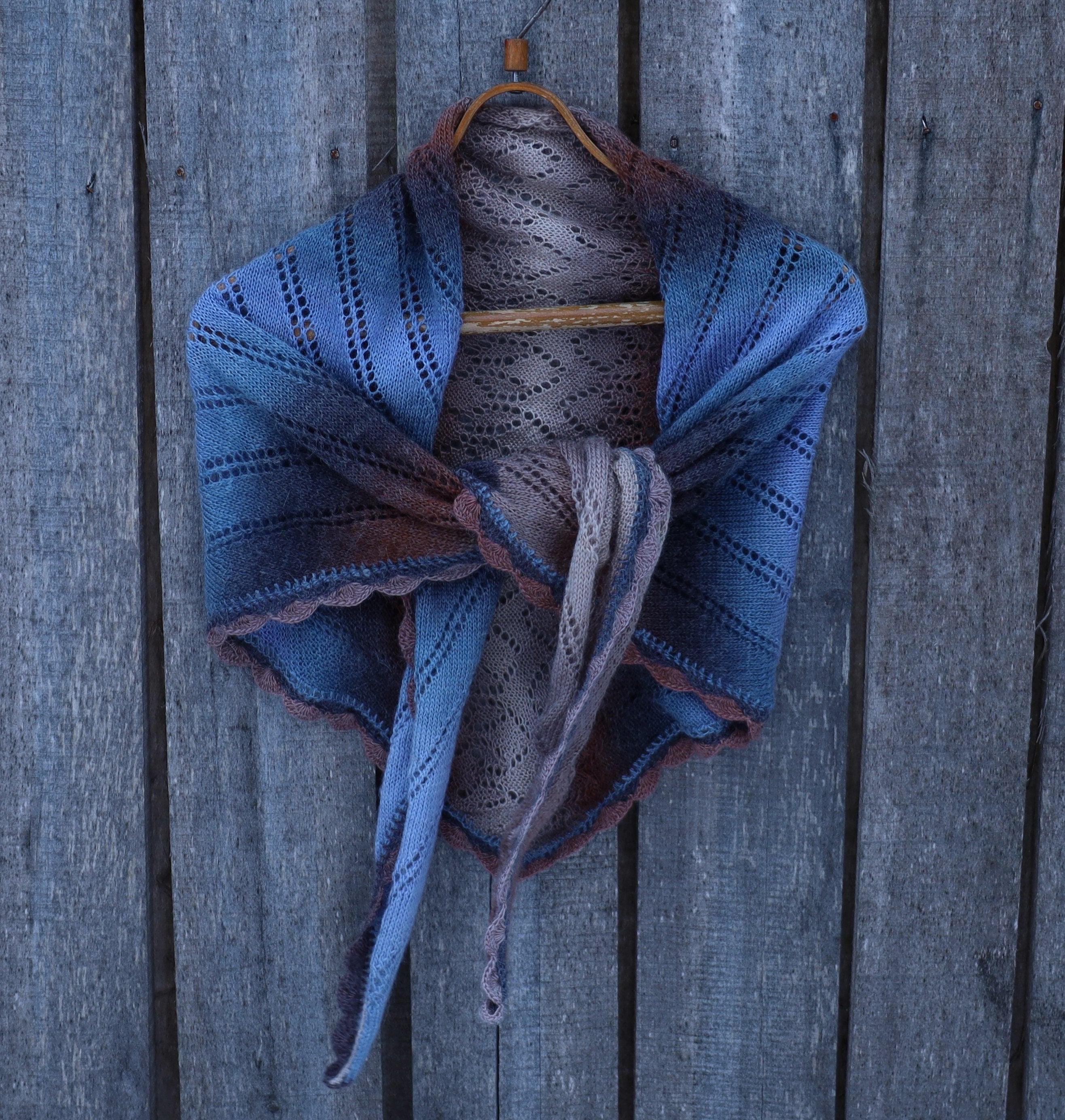 Blue knitted shawl on a wooden hanger against a wooden background