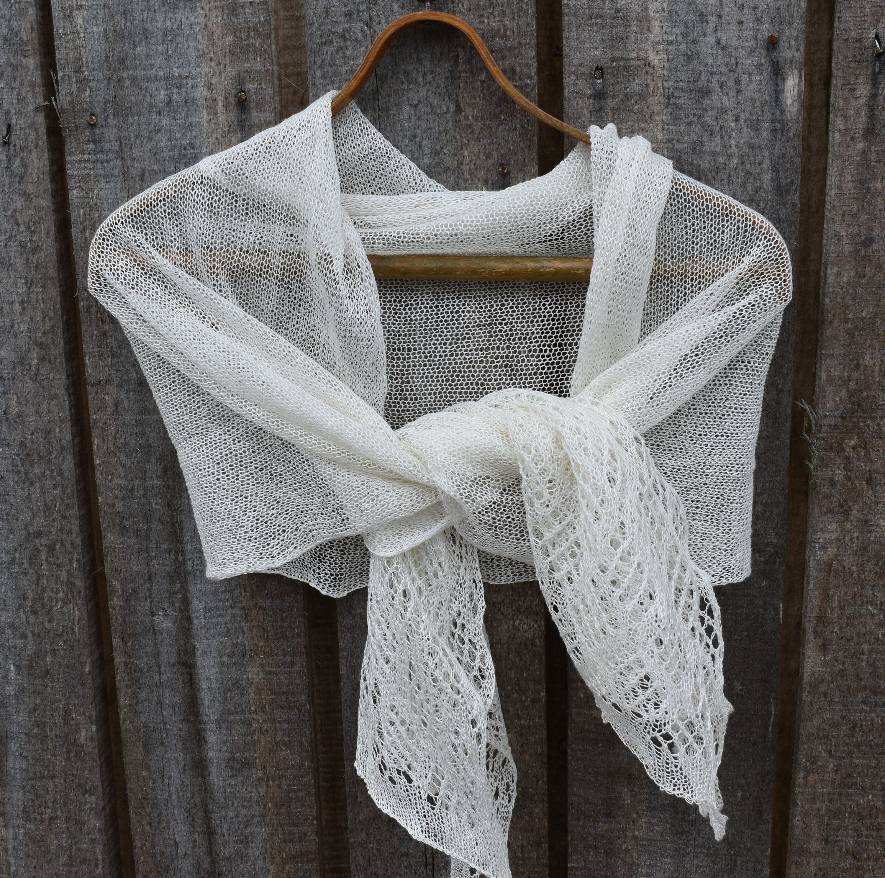 White lace shawl draped over a wooden hanger against a rustic wooden background