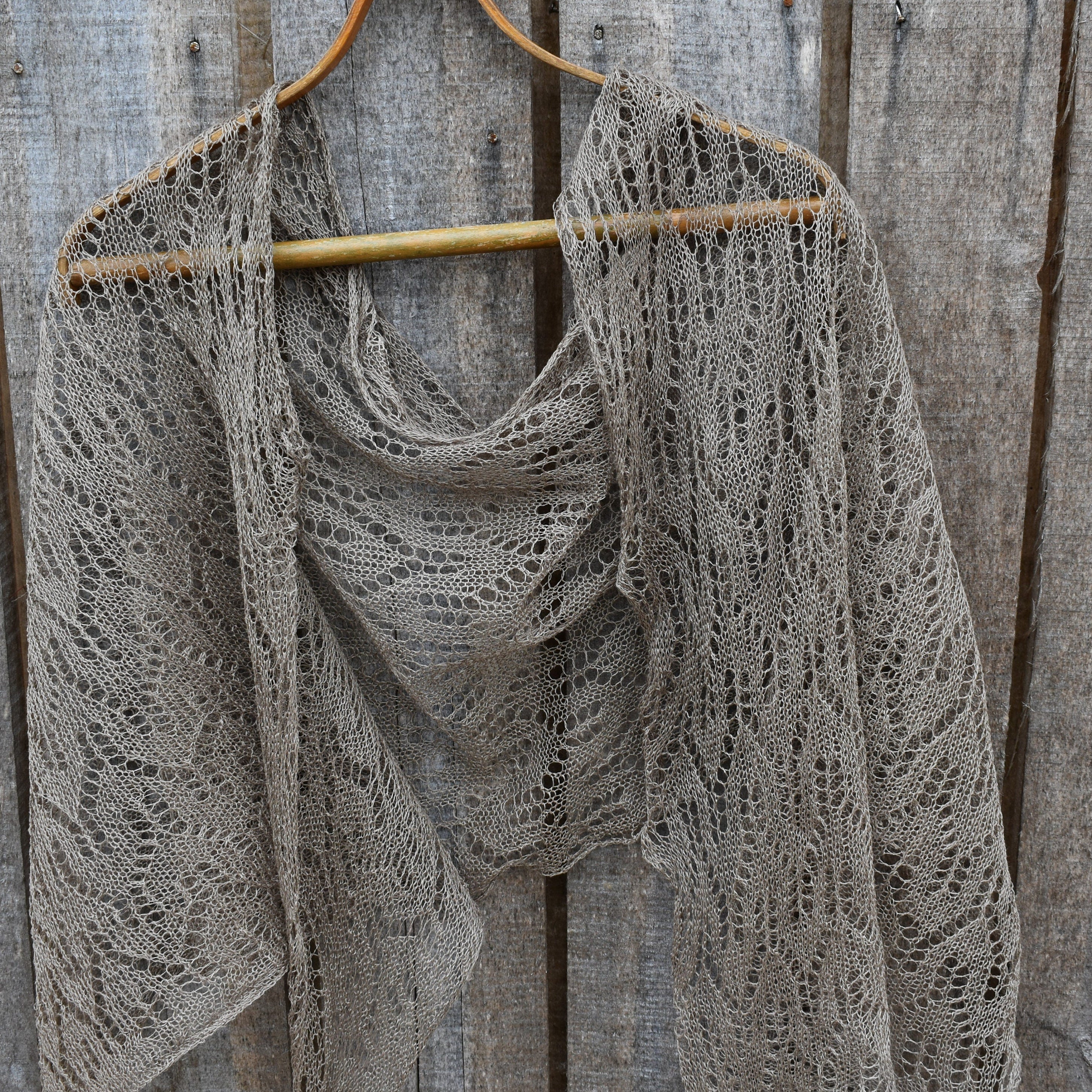 Knitted shawl on a wooden hanger against a rustic wooden background