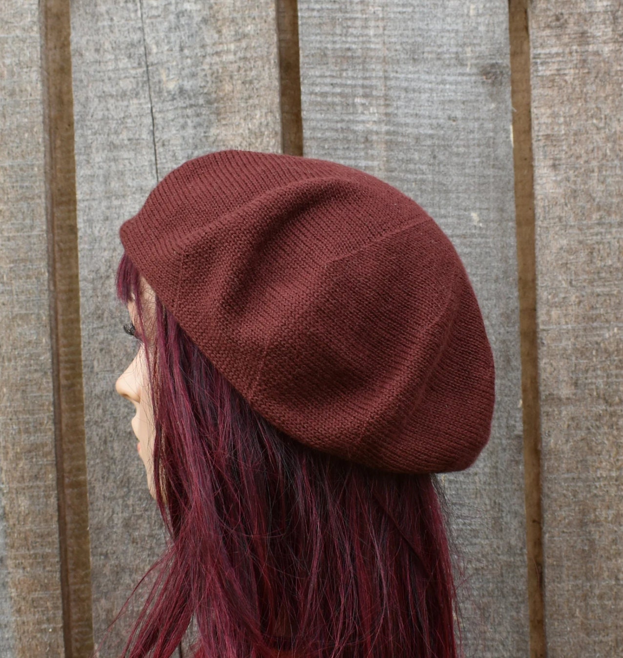 Person wearing a maroon knit beanie against a wooden background