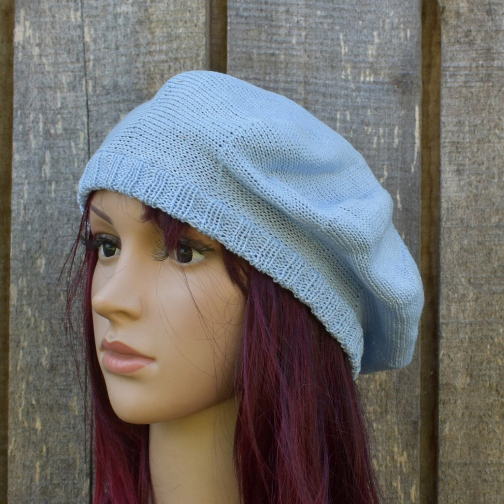 Mannequin head wearing a light blue knitted hat against a wooden background