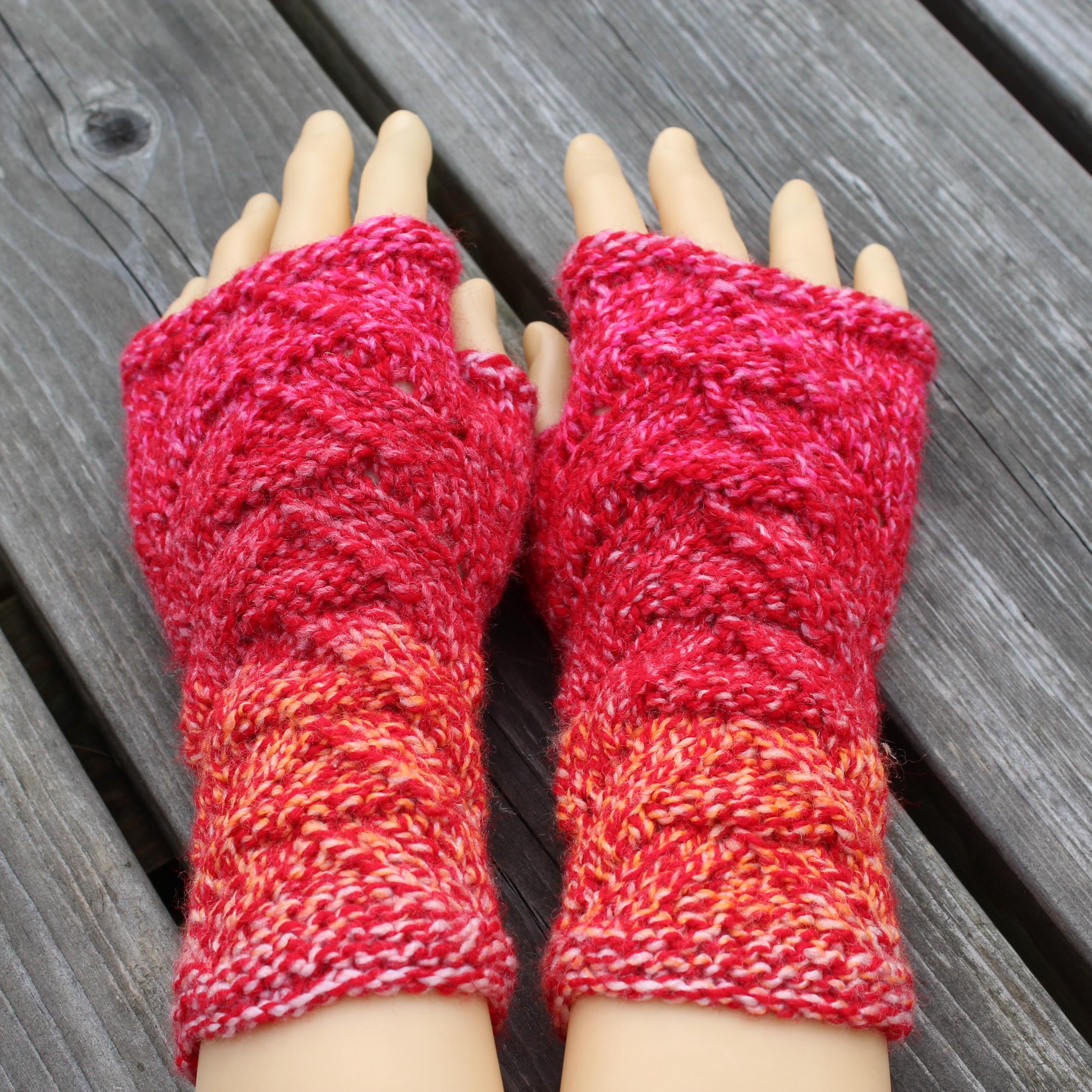 Red and orange knitted fingerless gloves on a wooden surface
