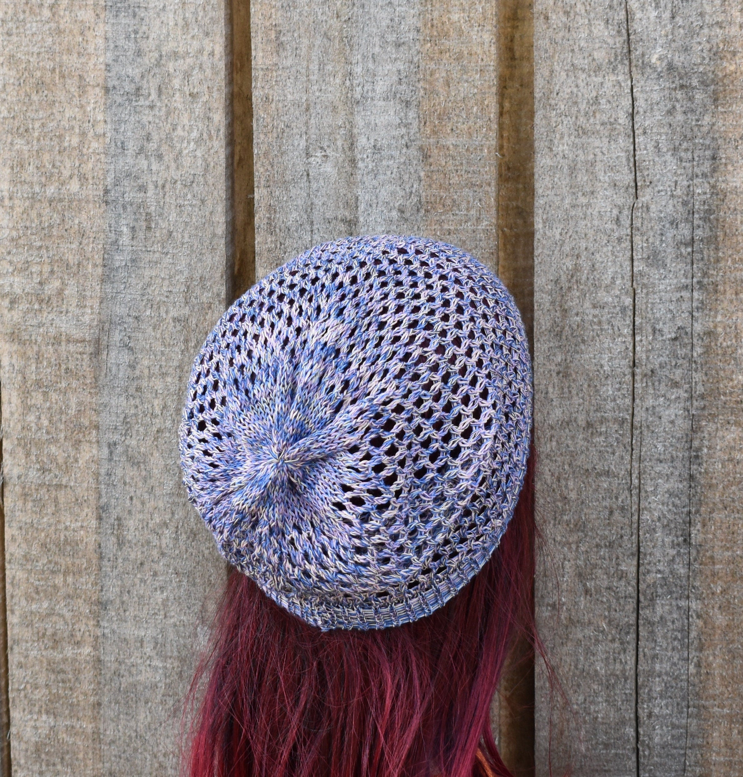 Blue knitted beret on a person with red hair against a wooden background