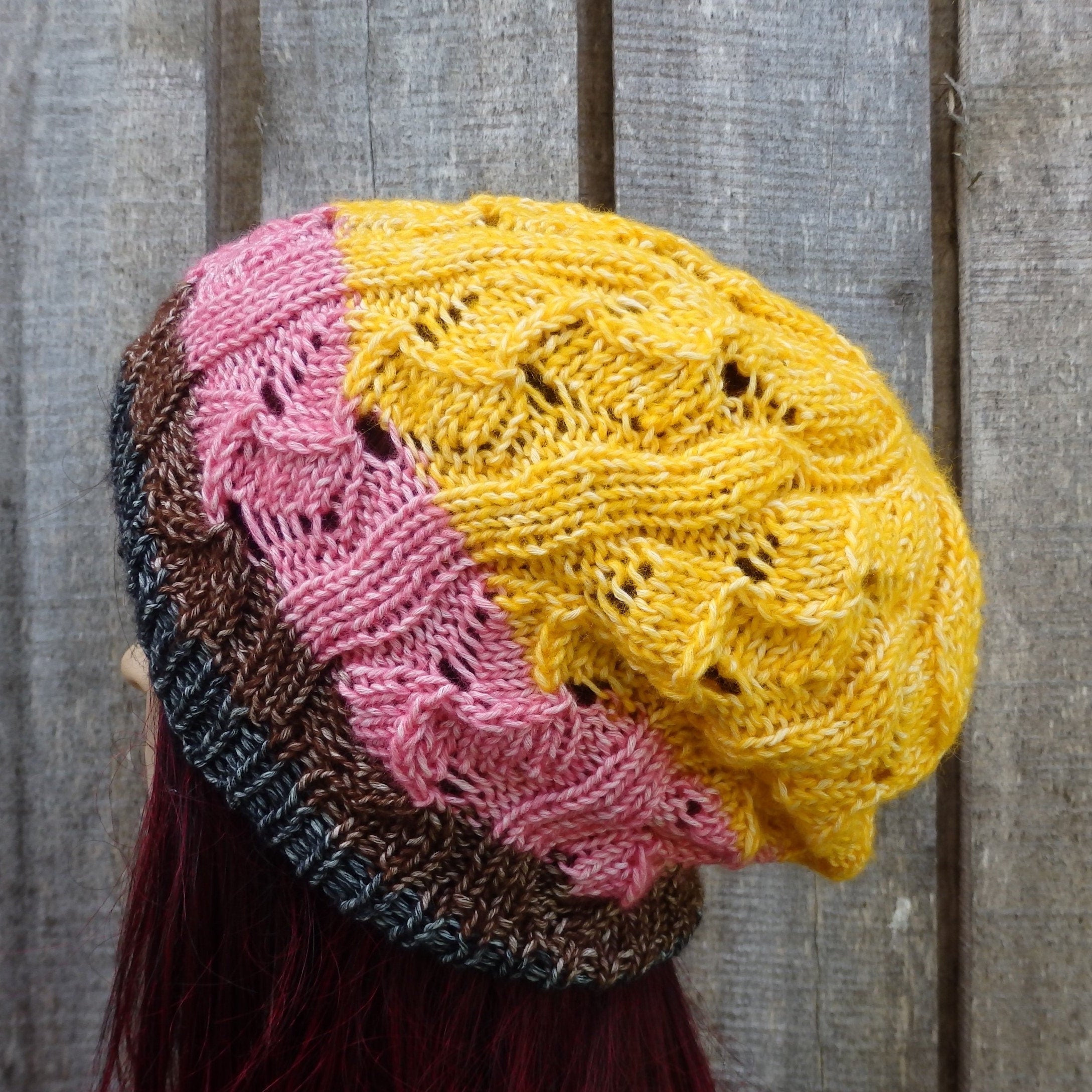 Multicolored knitted hat with pink, yellow, and black sections against a wooden background
