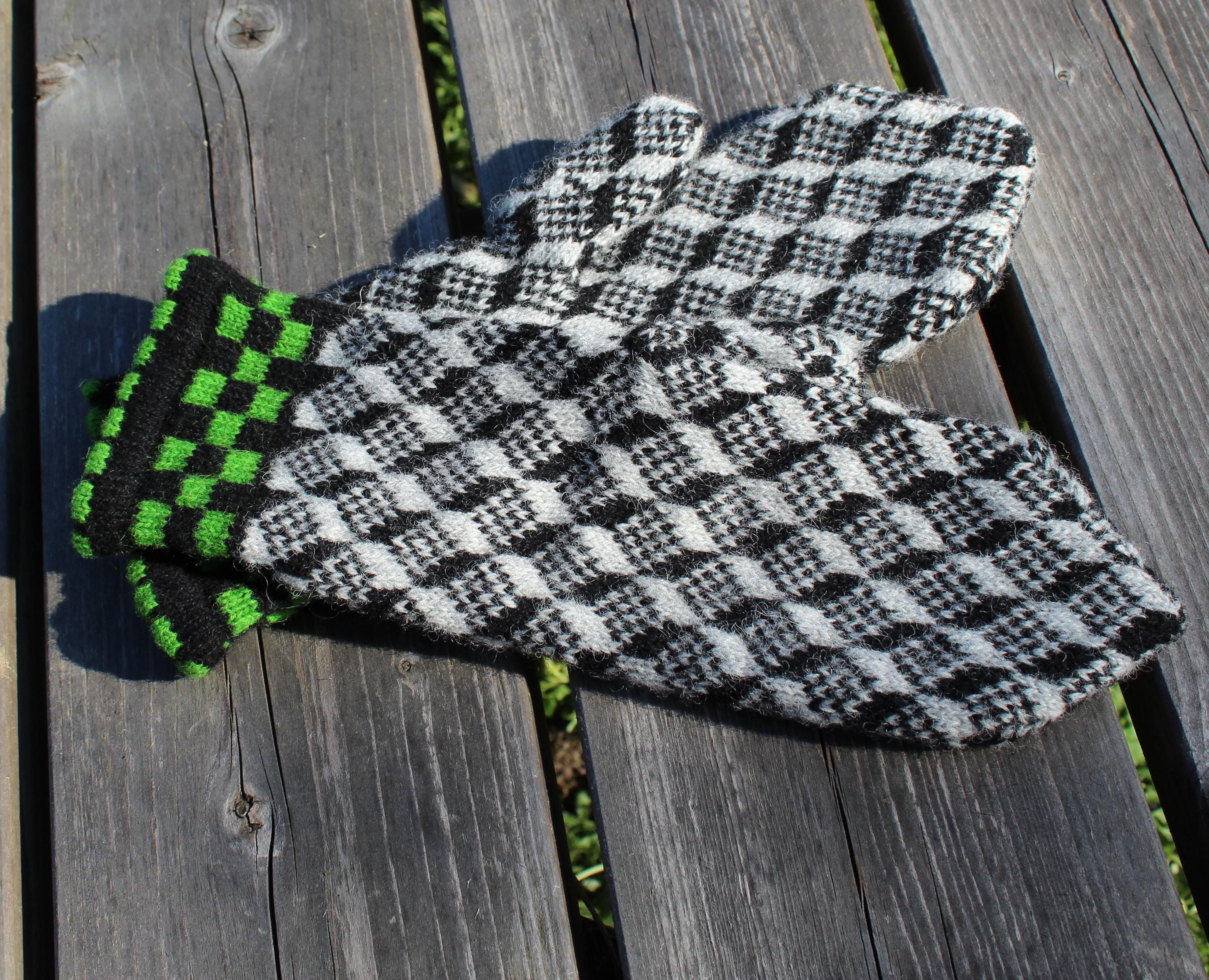 Pair of black and white checkered gloves with green cuffs on a wooden surface