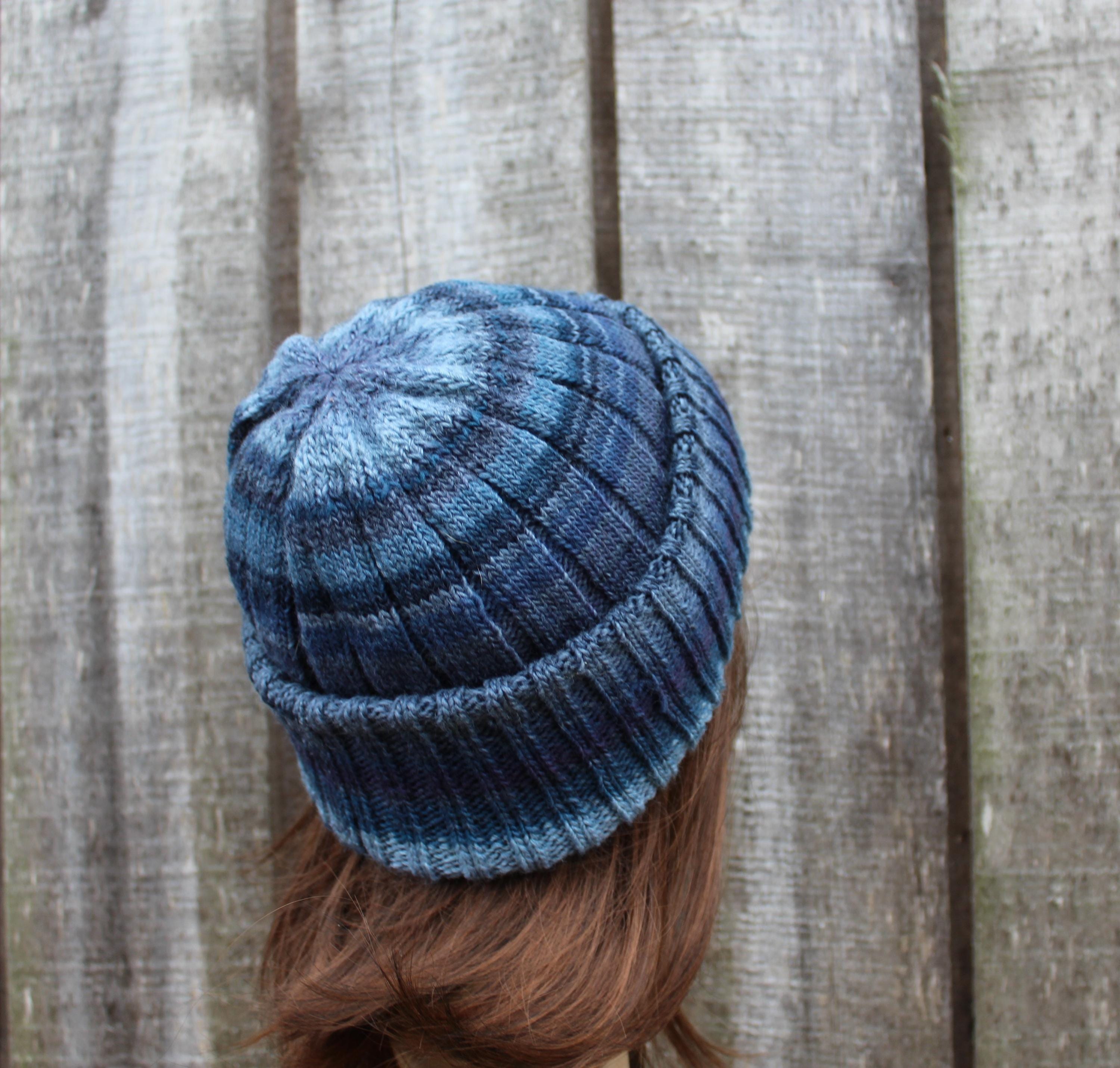 Blue knitted beanie worn by a person with brown hair against a wooden fence background