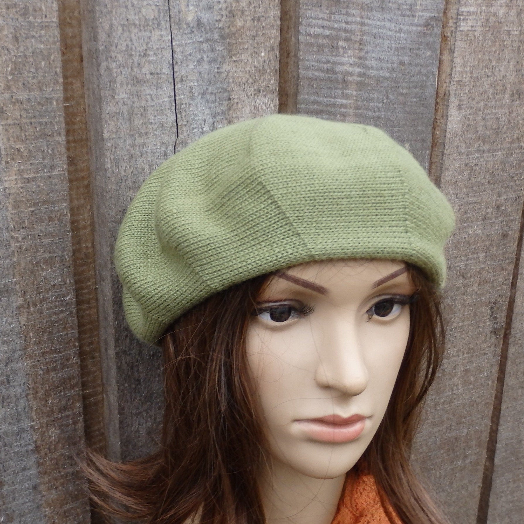 Green knitted beret on a mannequin head against a wooden background