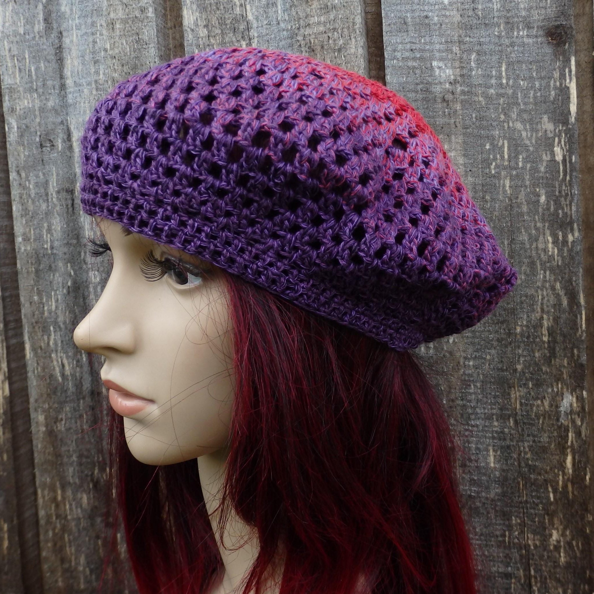 Mannequin head wearing a purple and red gradient crochet hat against a wooden background