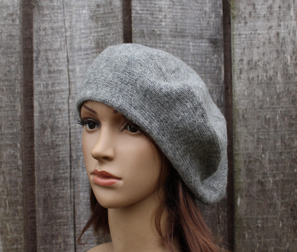 Mannequin head wearing a gray knit beret against a wooden fence background