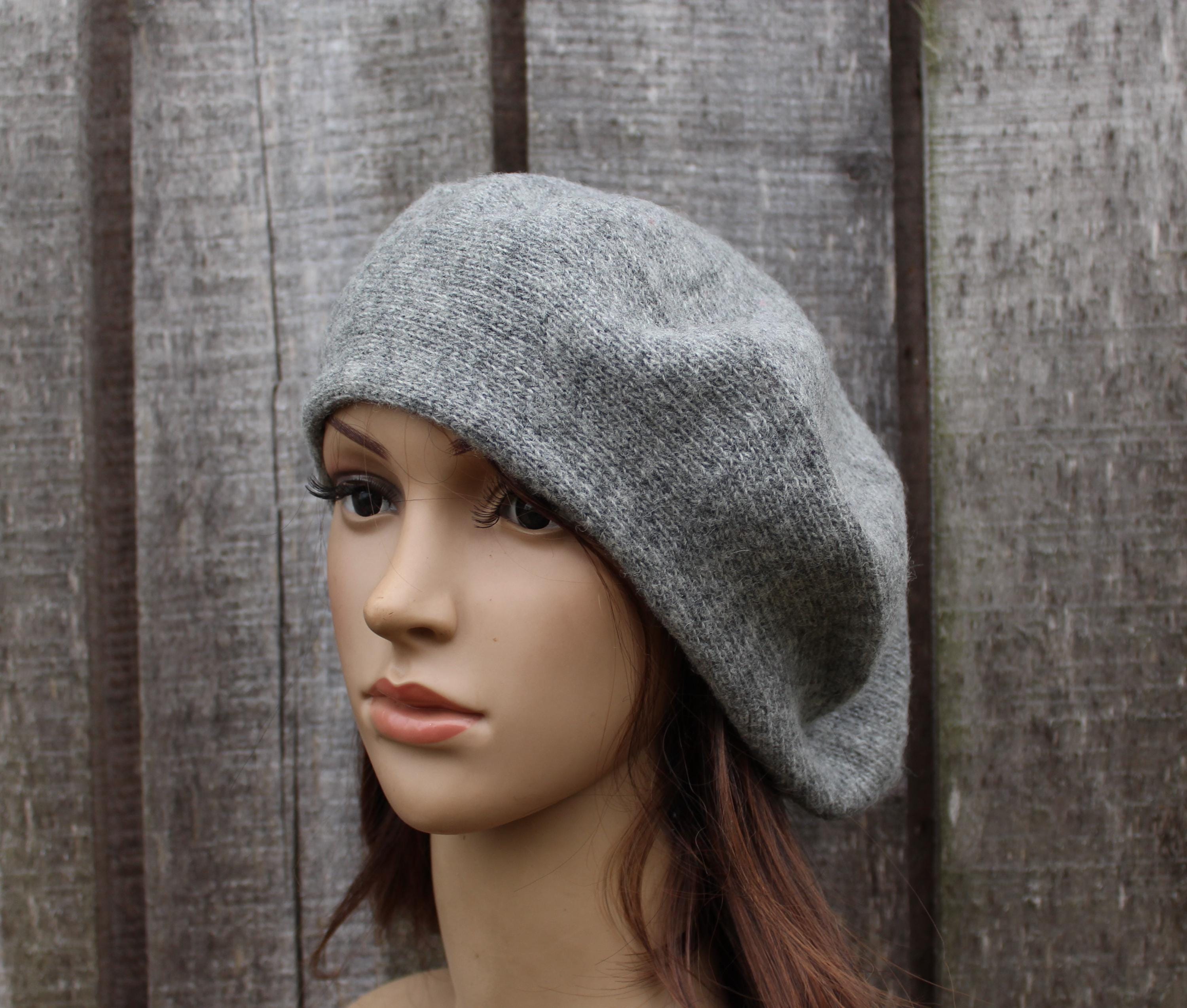 Mannequin head wearing a gray knit beret against a wooden fence background
