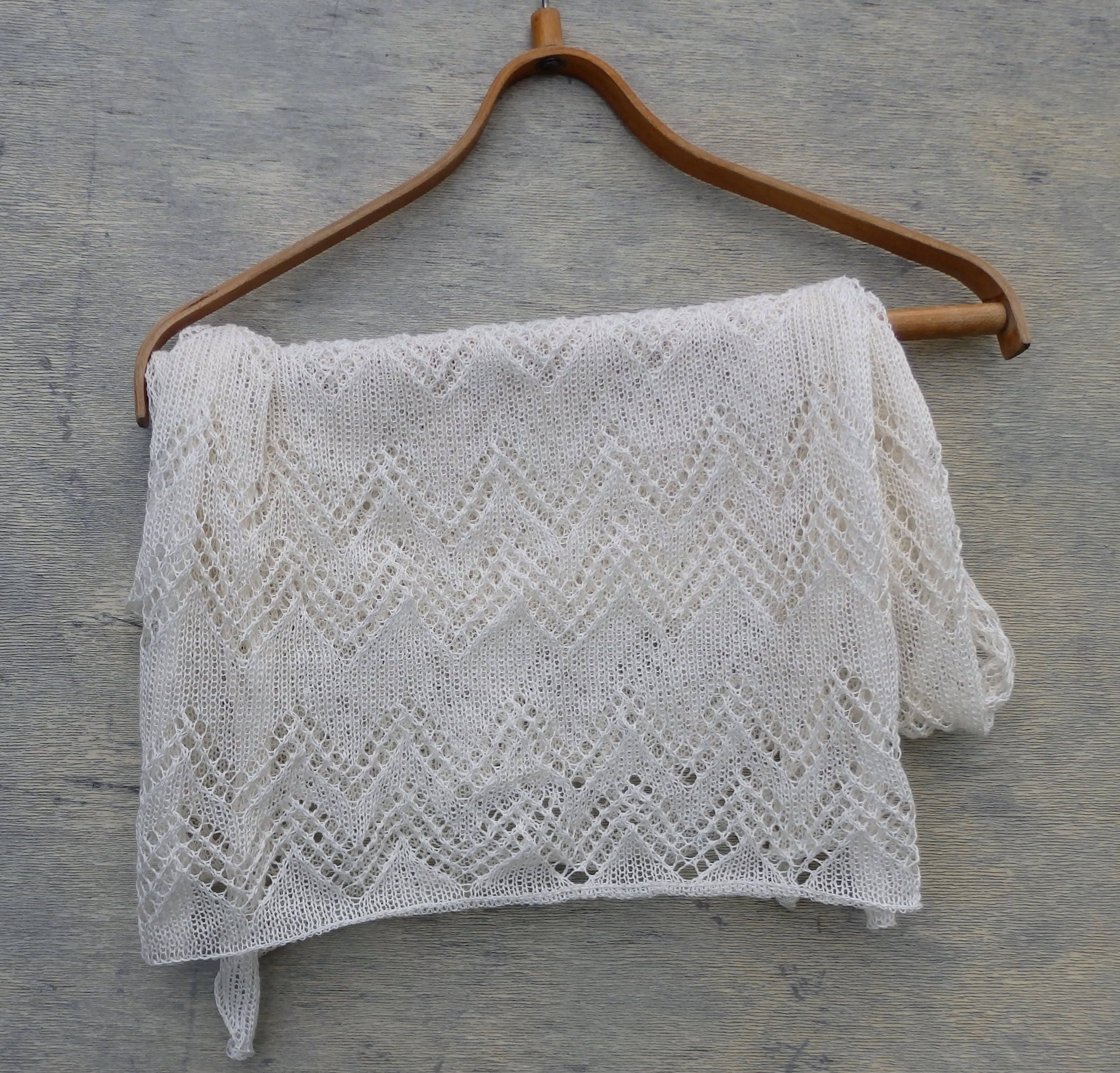 Knitted shawl with a diamond pattern draped over a wooden hanger on a gray surface
