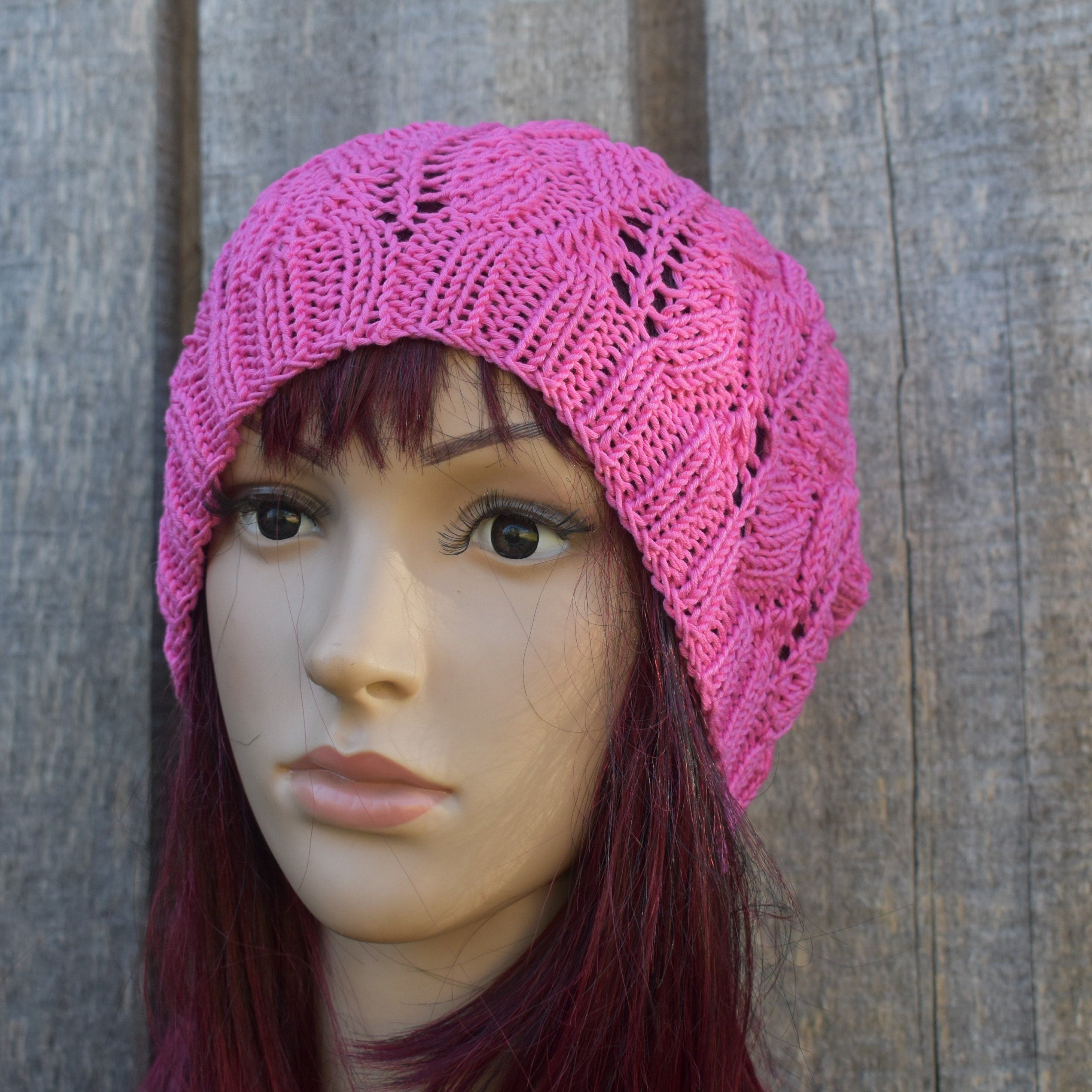 Mannequin head wearing a pink knitted hat against a wooden background