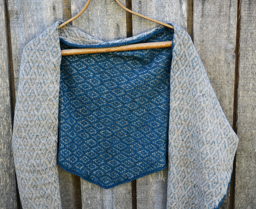 Textured blue and gray shawl on a wooden hanger against a wooden background