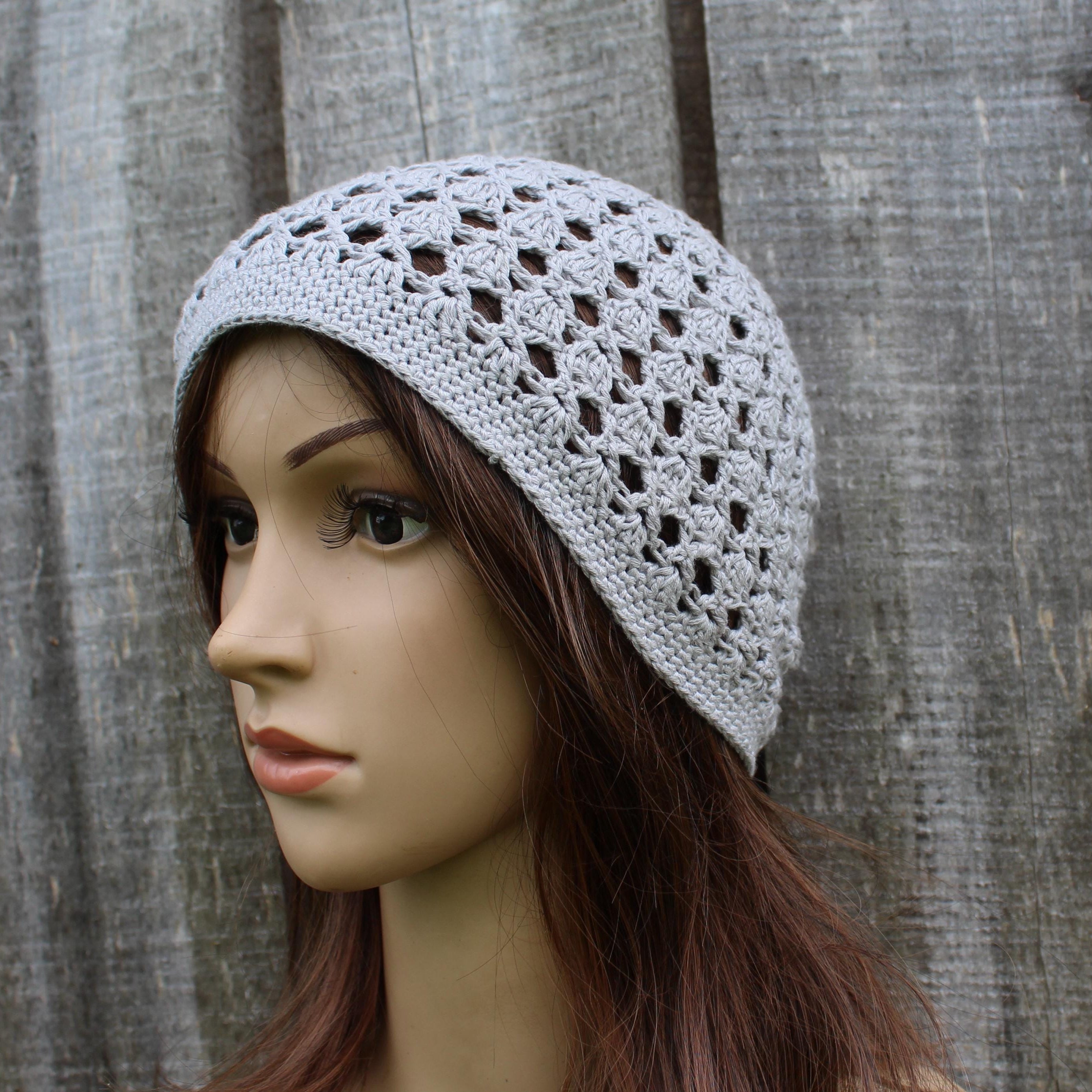 Mannequin head wearing a light gray crochet beanie against a wooden background