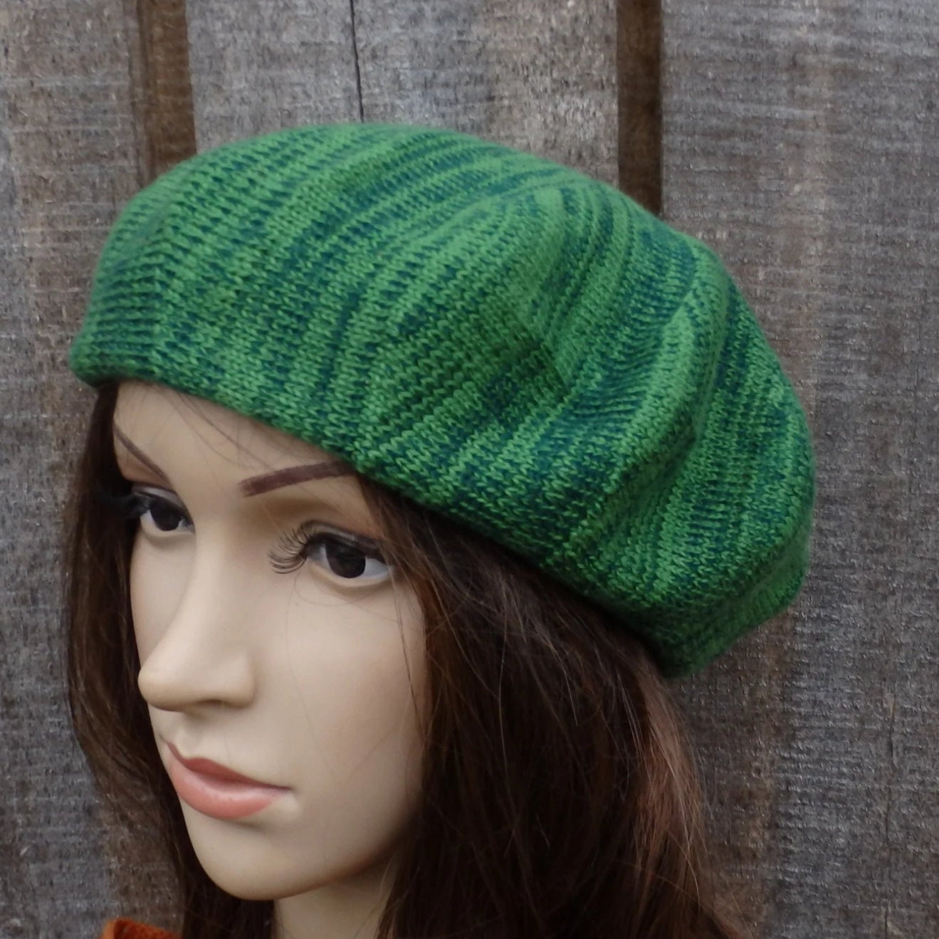 Green knitted beret on a mannequin head against a wooden background