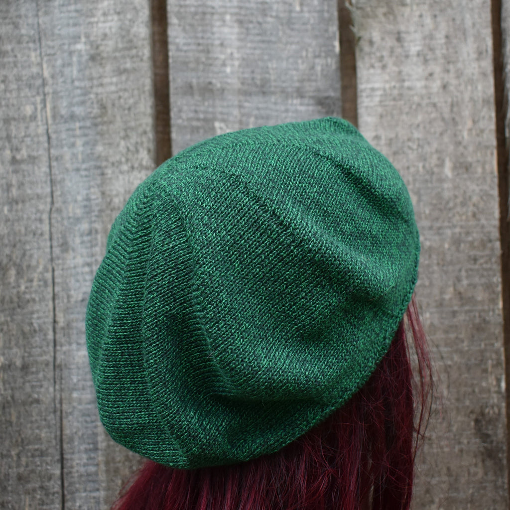 Green knitted beret on a person with red hair against a wooden background