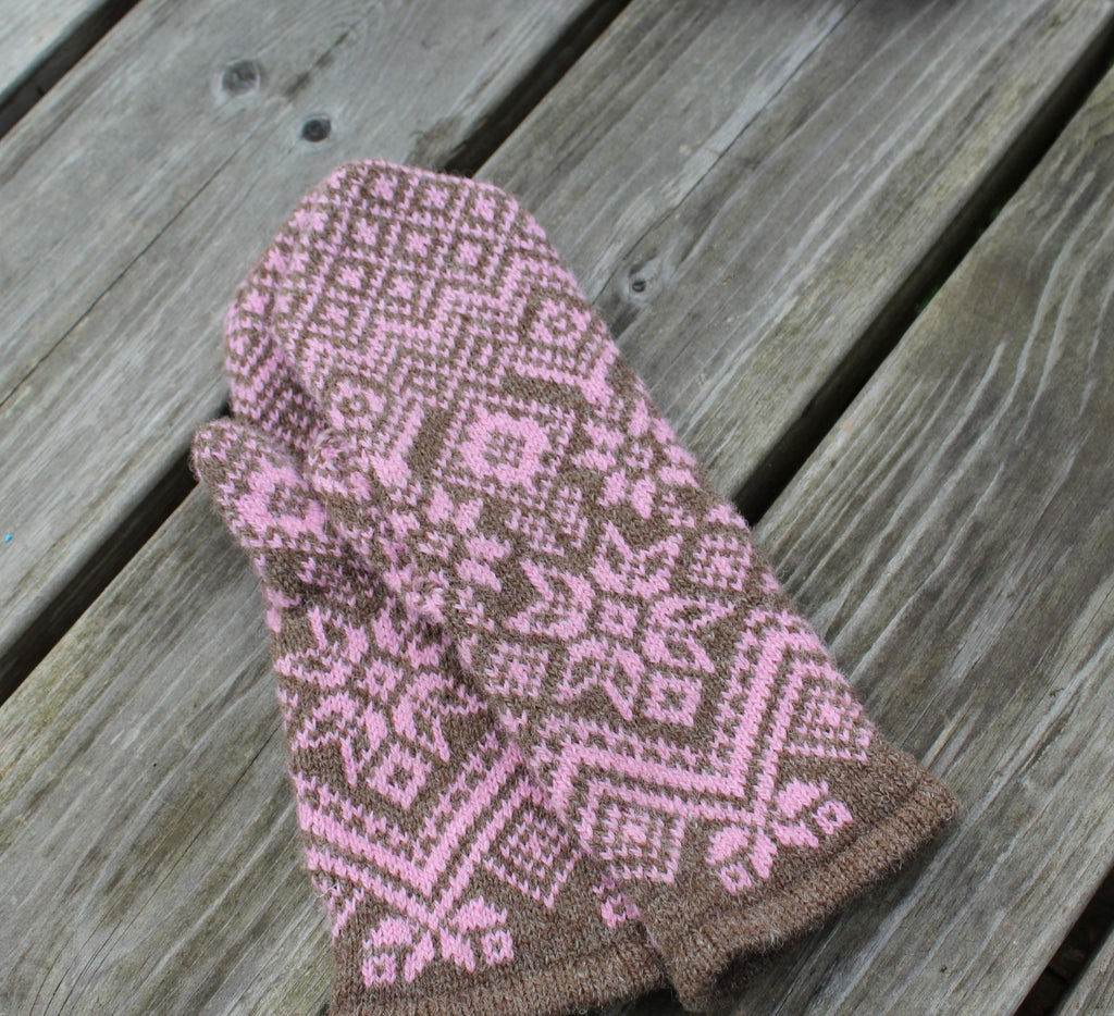 Knitted mitten with a pink and brown pattern on a wooden surface