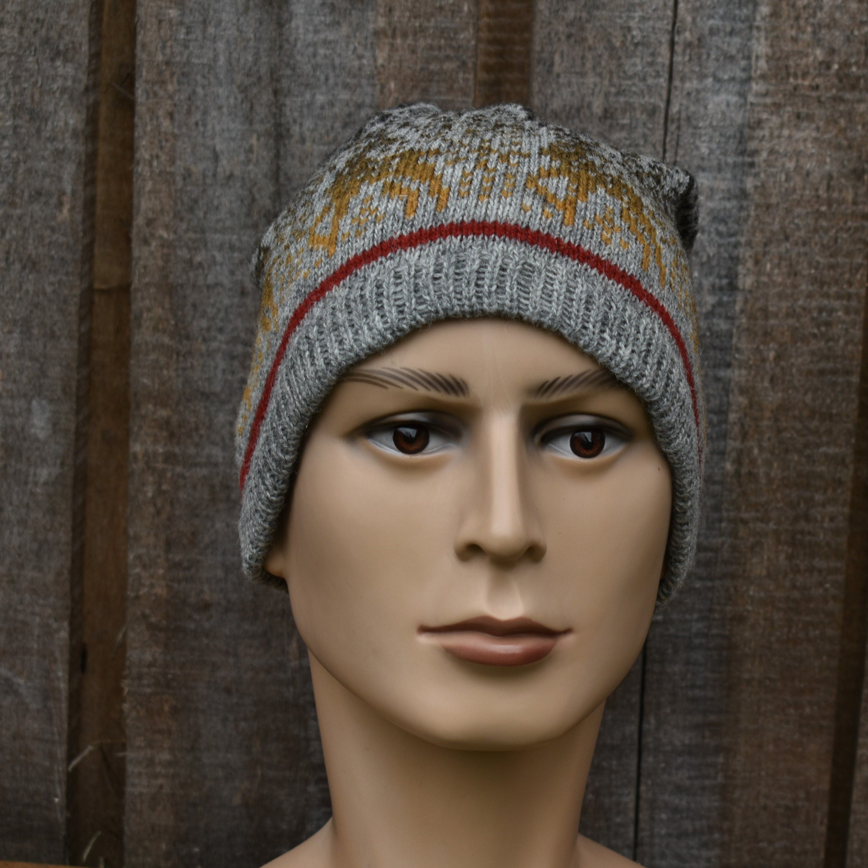 Mannequin head wearing a gray knit beanie with patterned design against a wooden background