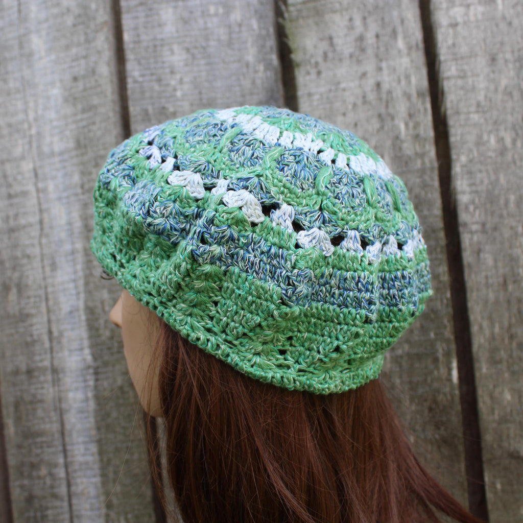 Green and white crocheted beanie on a mannequin head against a wooden background