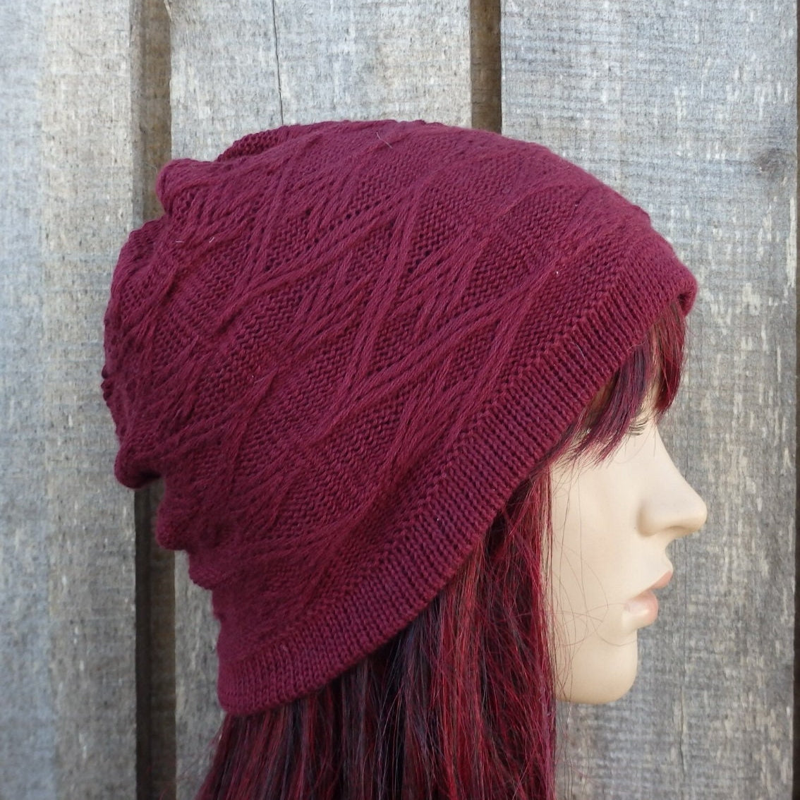Maroon knitted beanie worn by a person with red hair against a wooden background