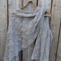 Gray knitted shawl on a wooden hanger against a wooden background