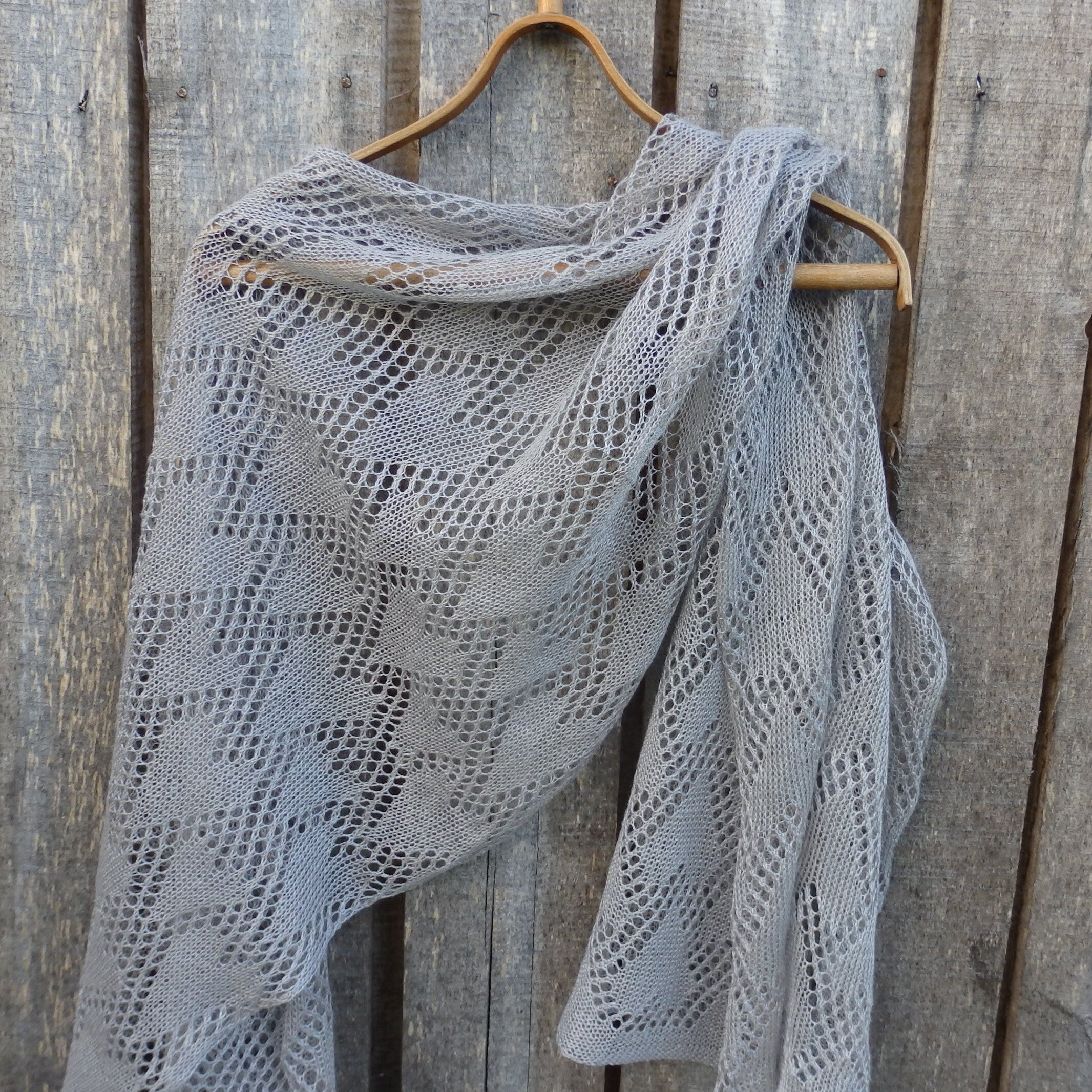 Gray knitted shawl on a wooden hanger against a wooden background