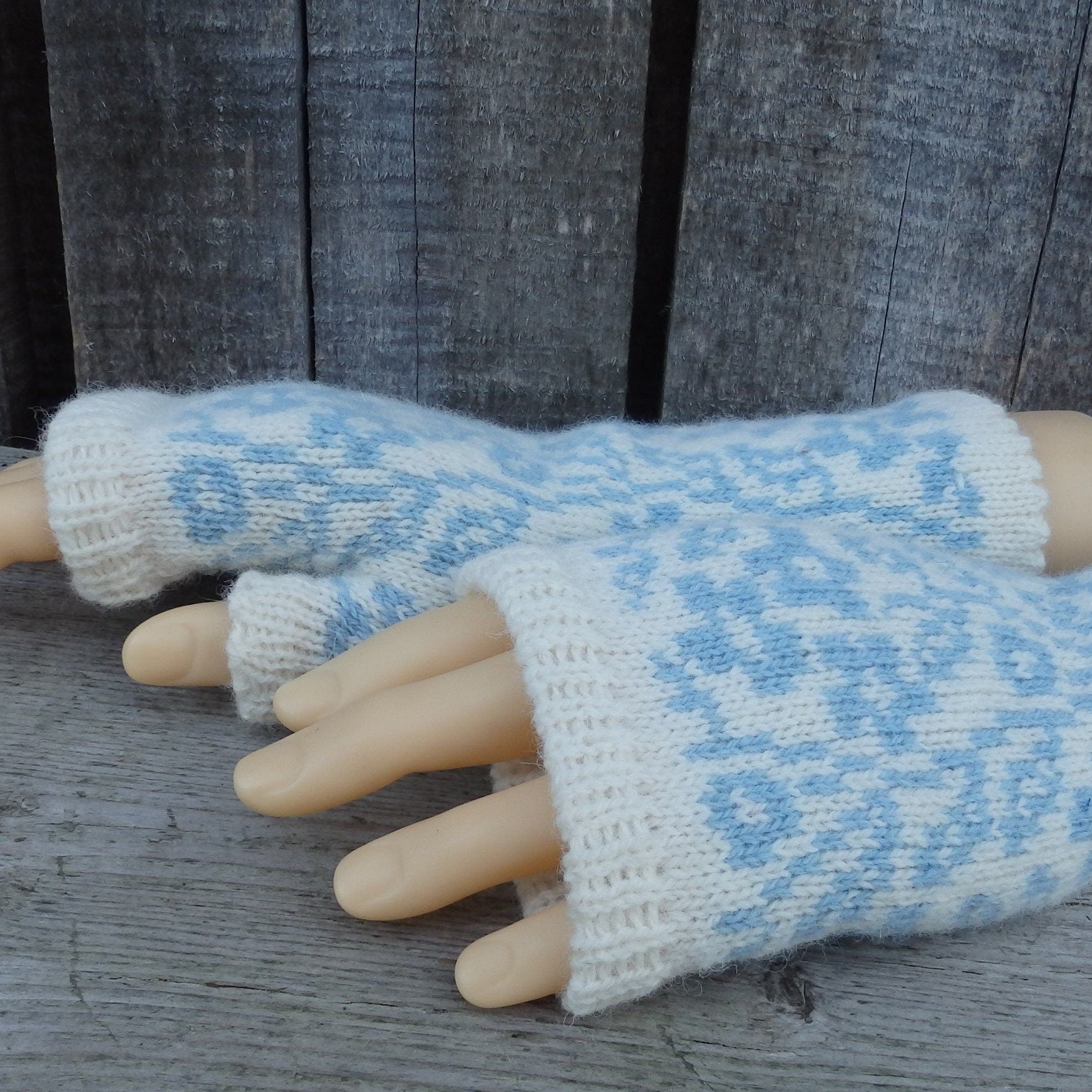 Pair of light blue and white patterned fingerless gloves on a wooden surface