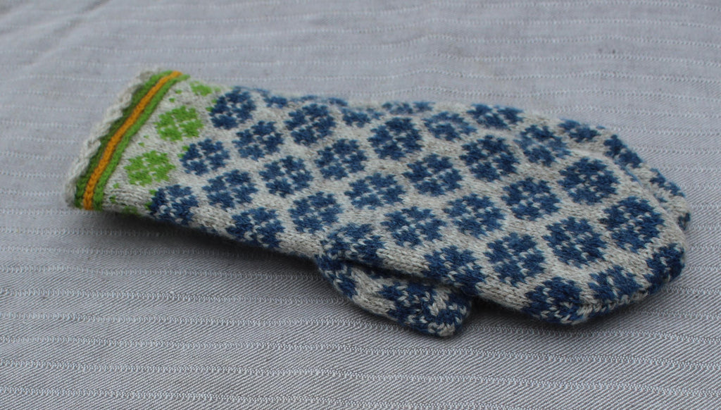 Knitted mittens with blue and green pattern on a gray fabric background