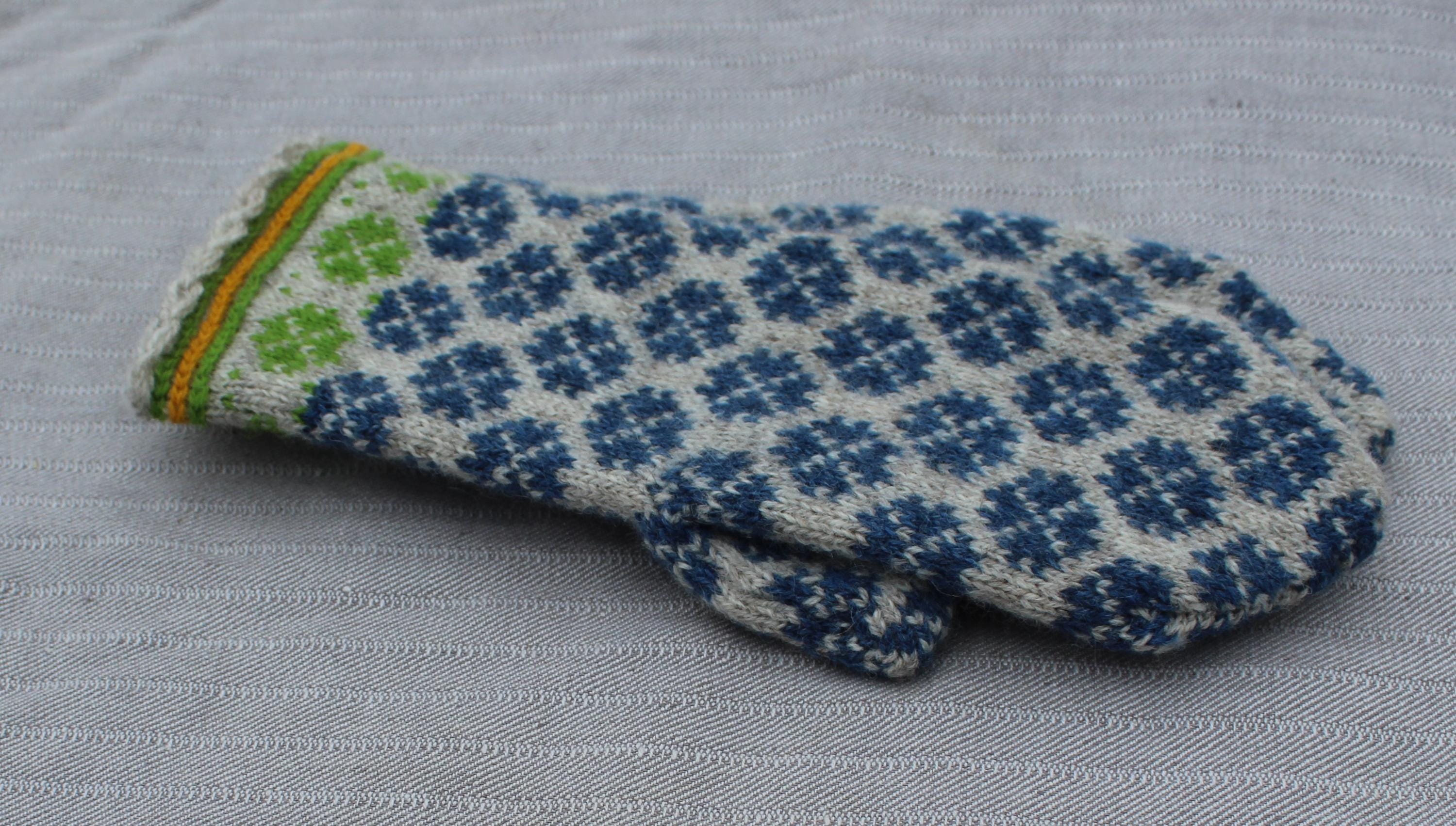 Knitted mittens with blue and green pattern on a gray fabric background