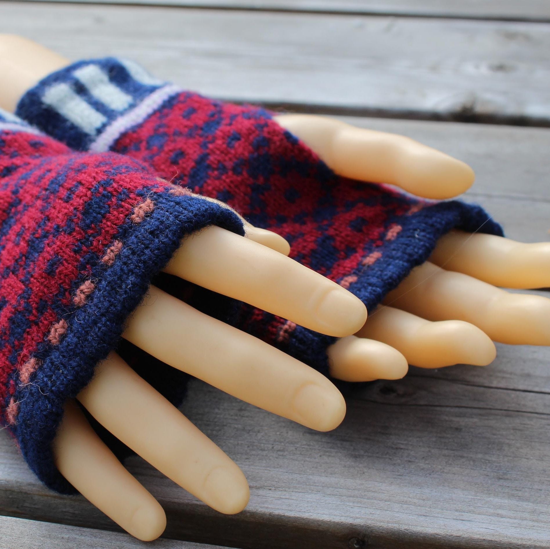 Pair of knitted fingerless gloves on a mannequin hand against a wooden background