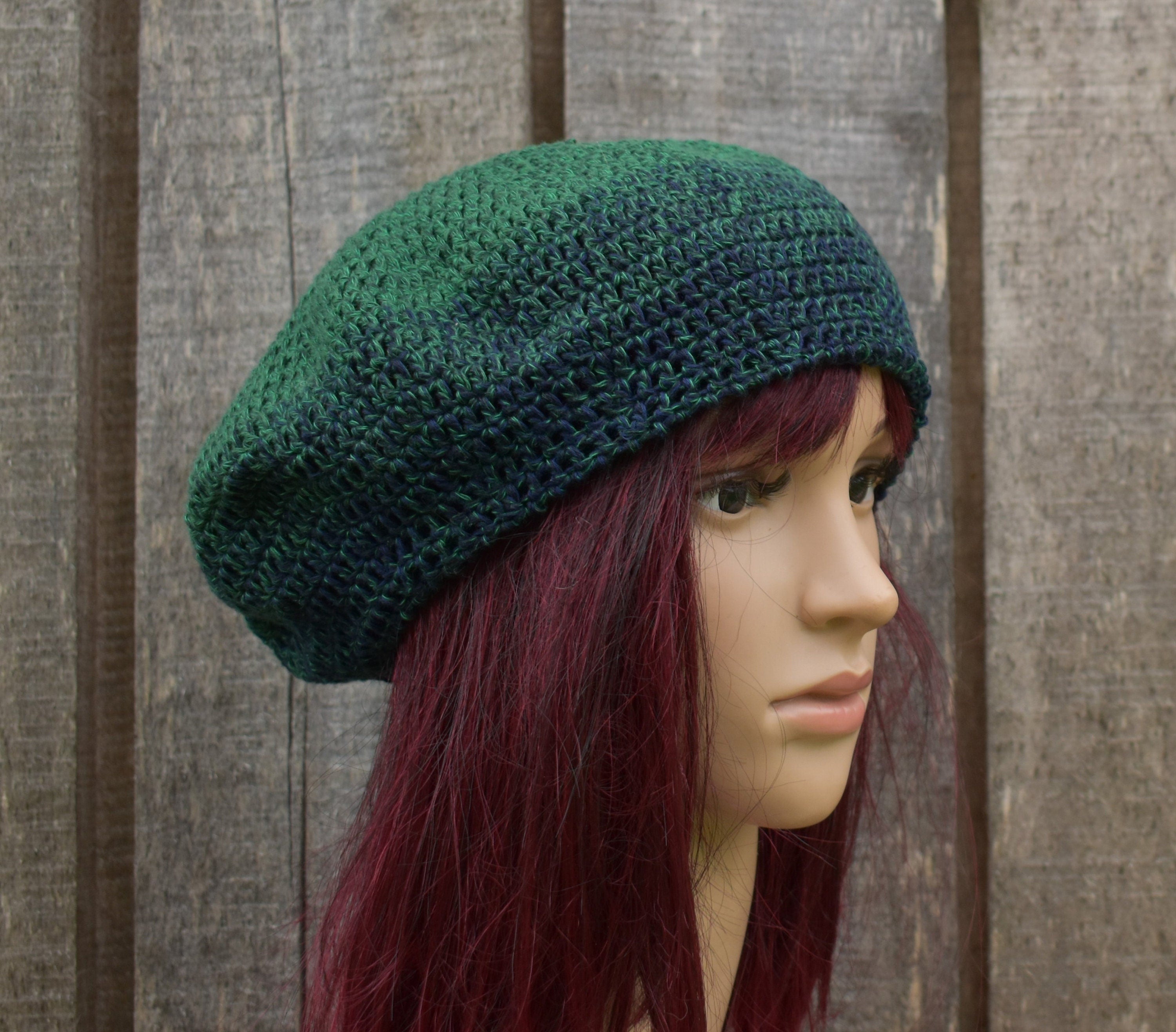 Green knitted beret worn by a mannequin against a wooden background