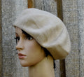 Beige knitted beret on a mannequin head against a textured wall.