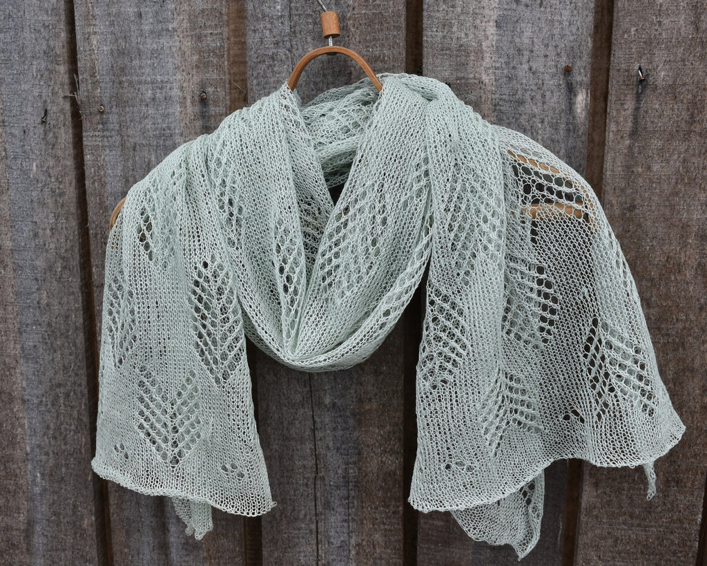 Knitted shawl with a lace pattern draped over a wooden hook against a wooden background
