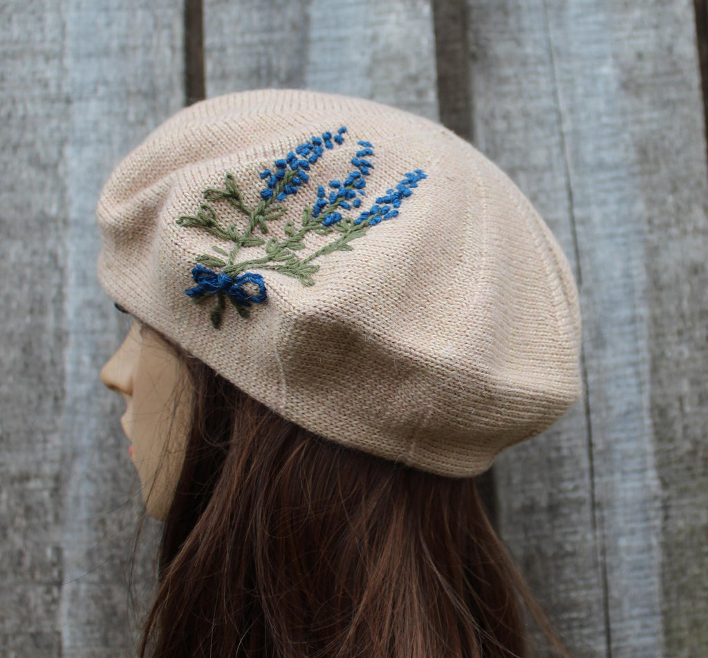 Beige beret with embroidered blue flowers on a wooden background
