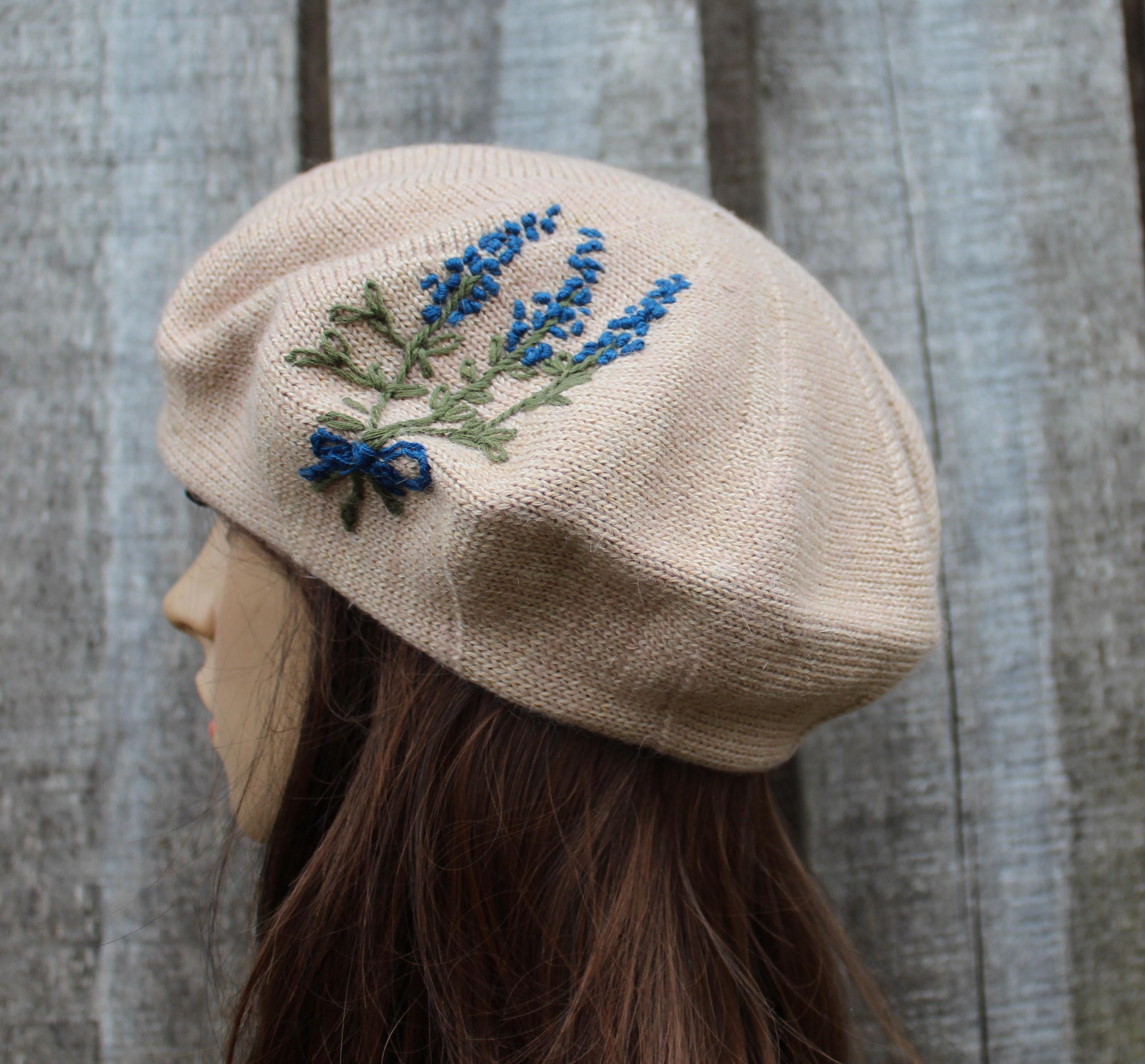 Beige beret with embroidered blue flowers on a wooden background
