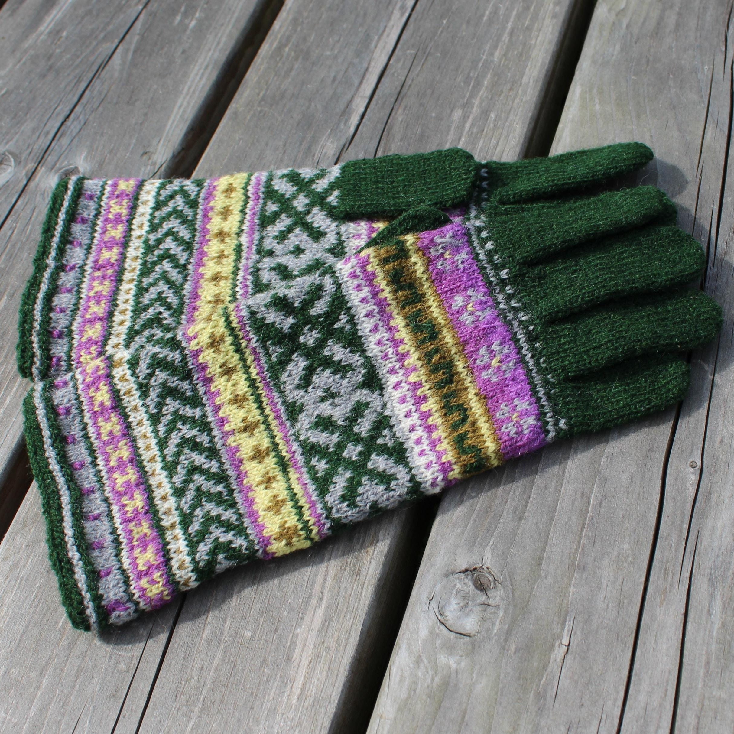 Pair of green gloves with colorful pattern on a wooden surface
