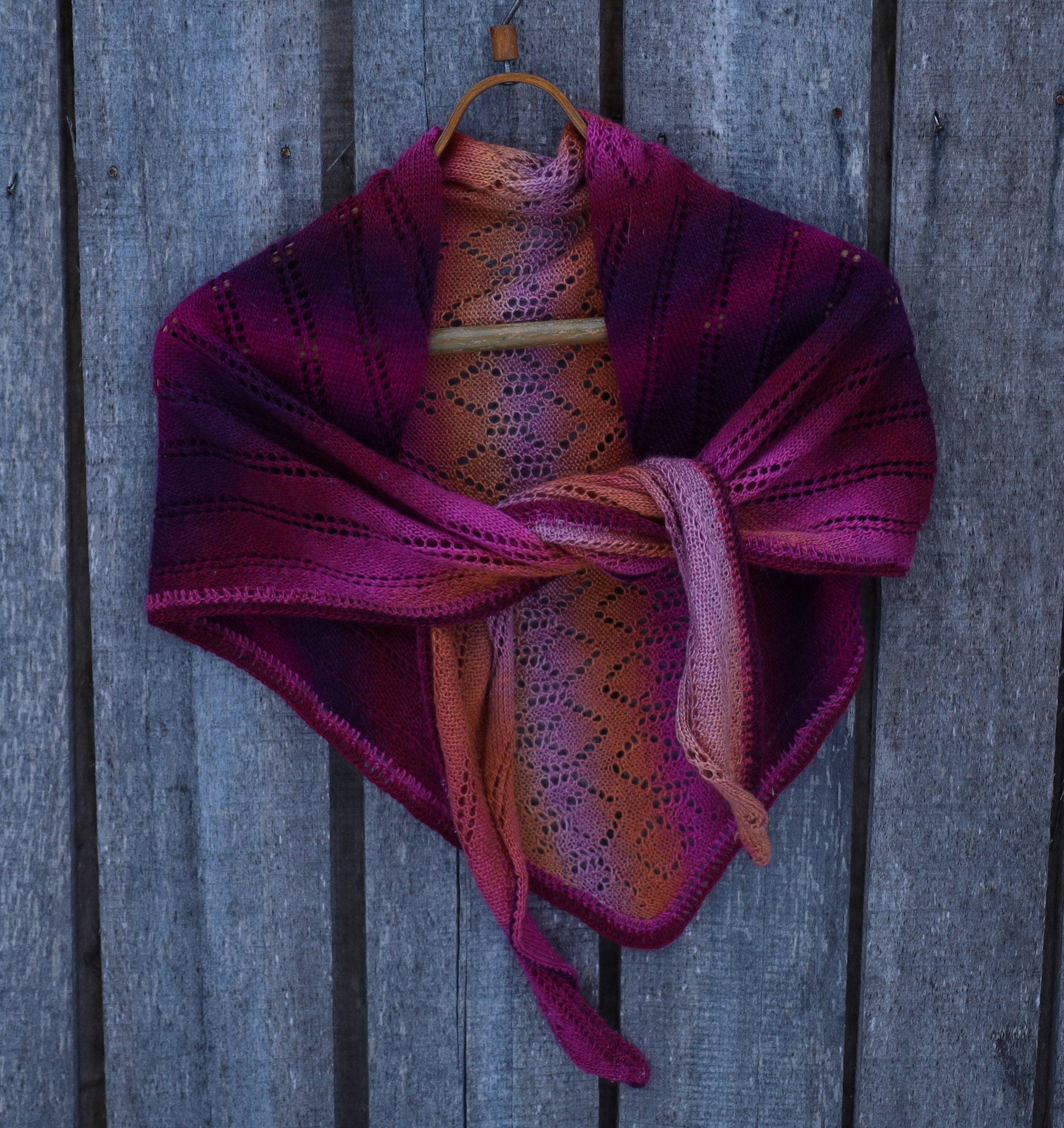 Knitted shawl with purple and orange gradient draped over a wooden surface