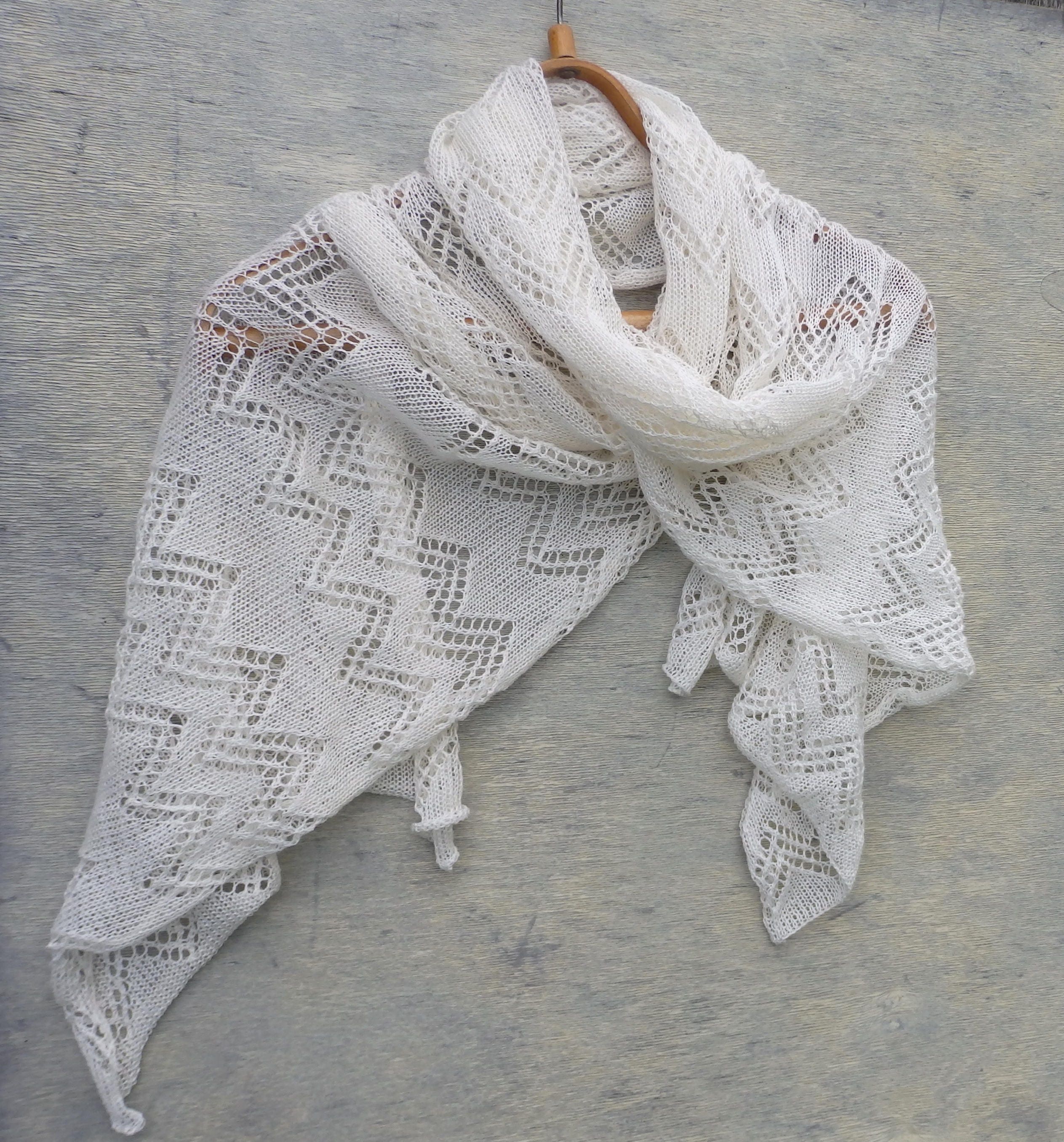 White lace shawl on a wooden hanger against a gray background