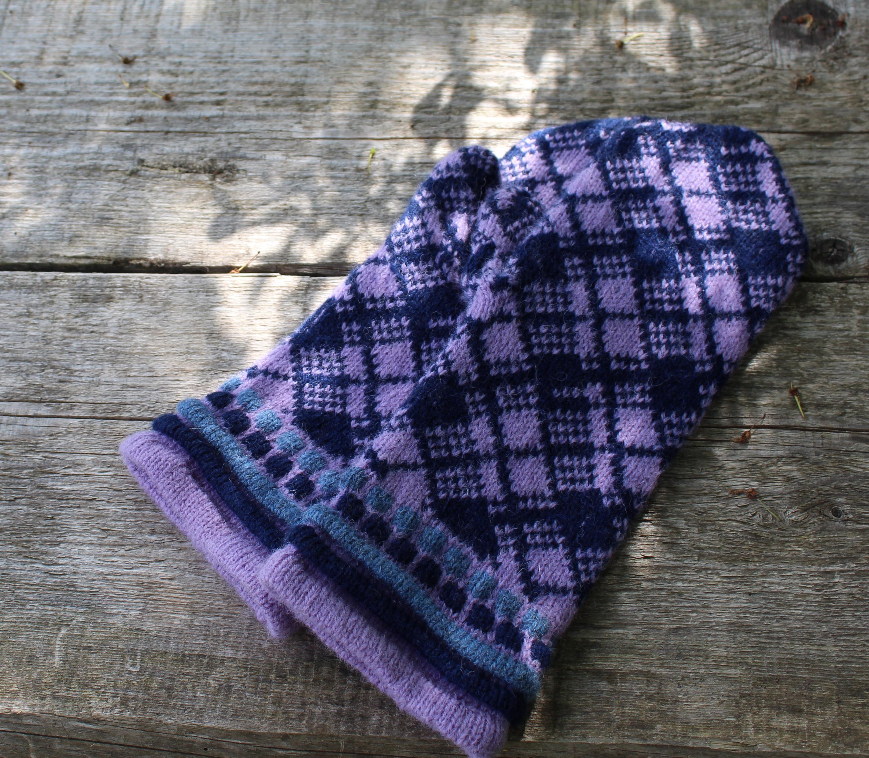 Pair of purple and blue plaid mittens on a wooden surface