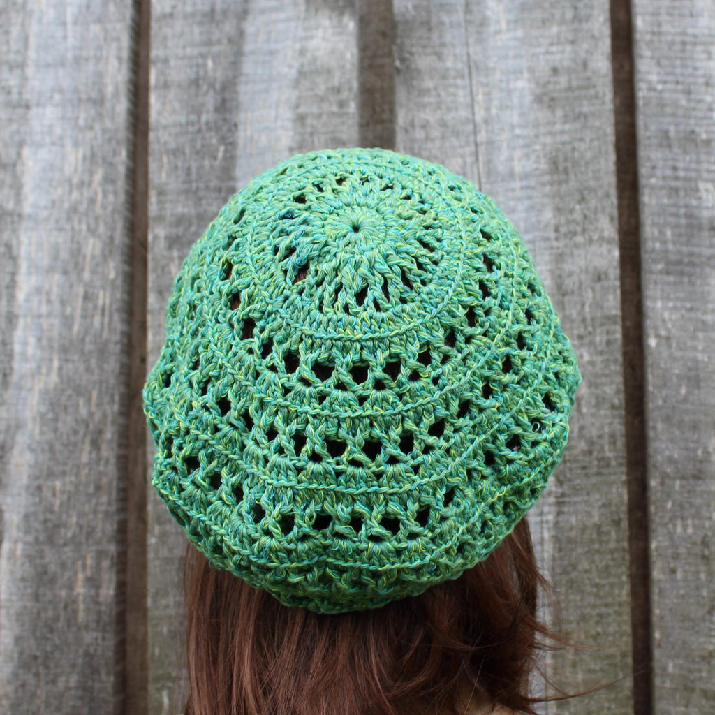Green crocheted beanie worn by a person against a wooden background