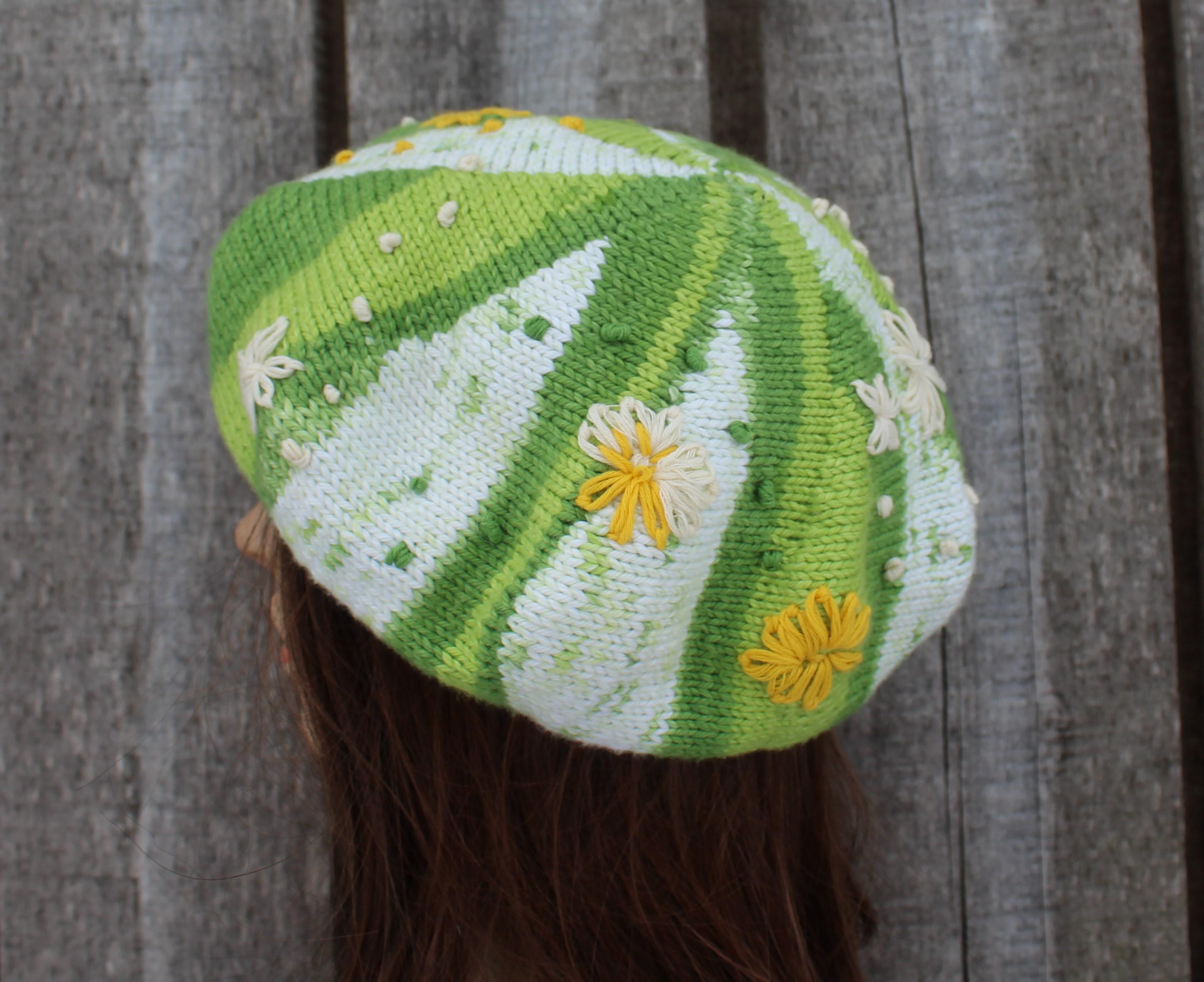 Knitted hat with green and white pattern and yellow flowers against a wooden background