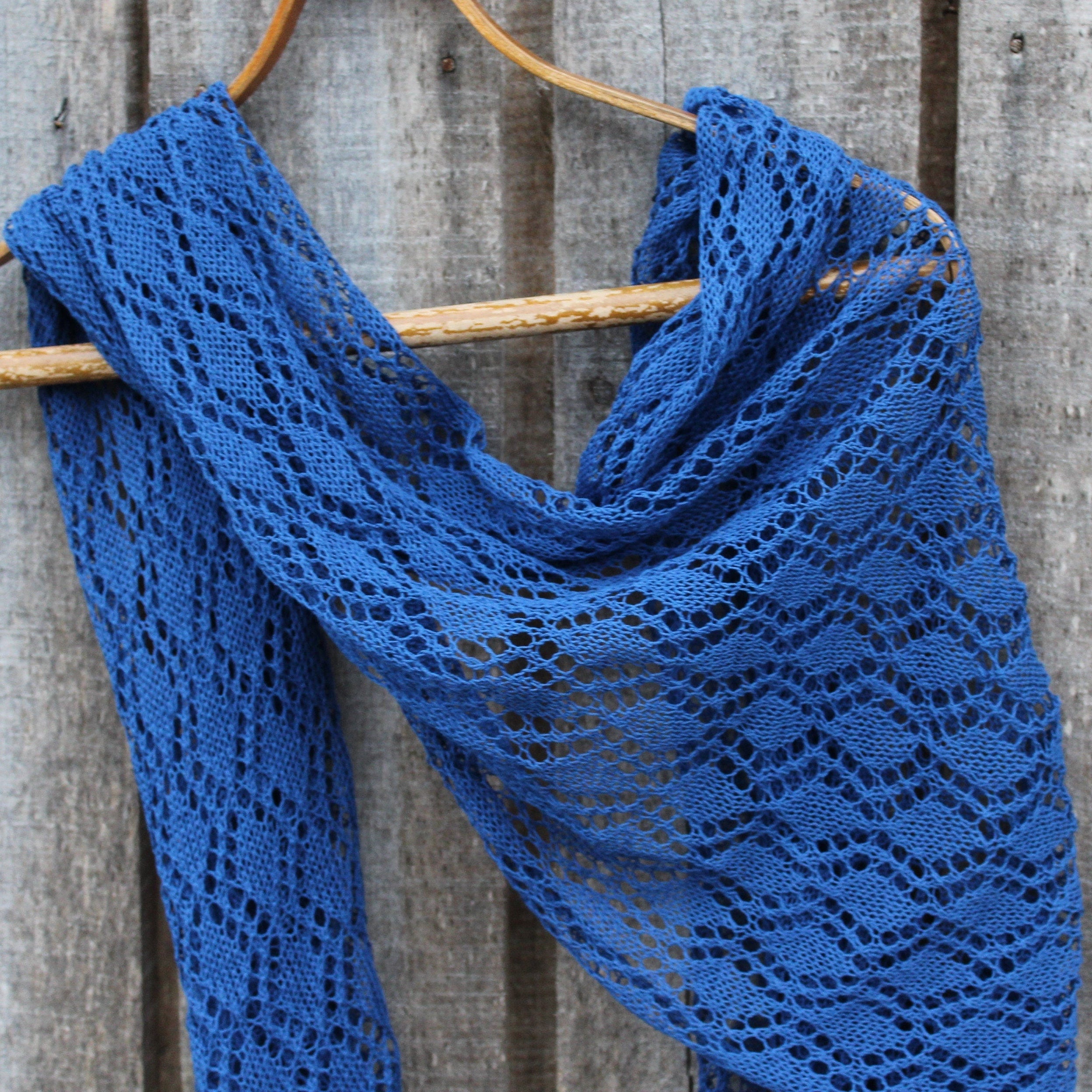 Blue knitted scarf on a wooden hanger against a rustic wooden background