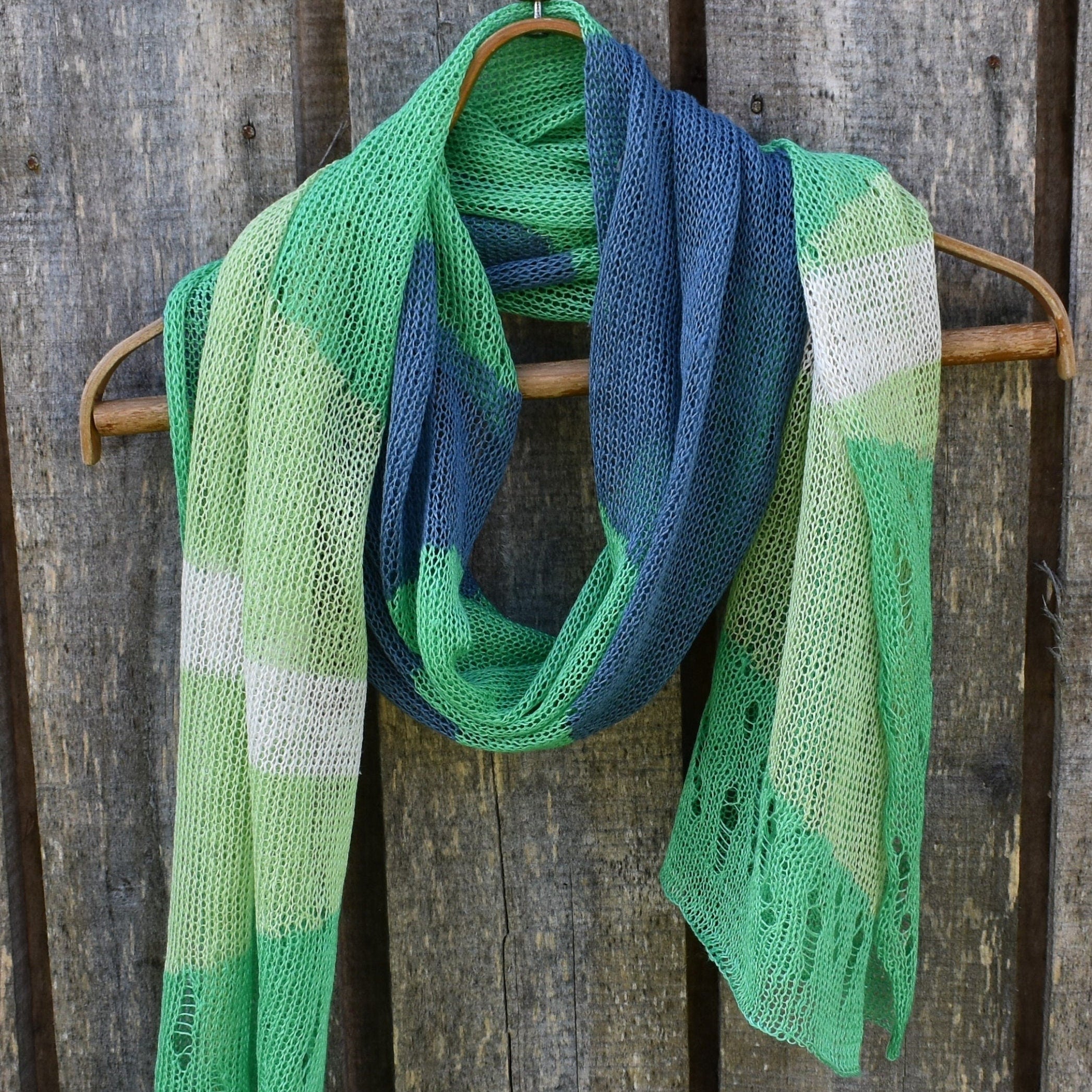 Knitted scarf with green and blue pattern hanging on a wooden surface