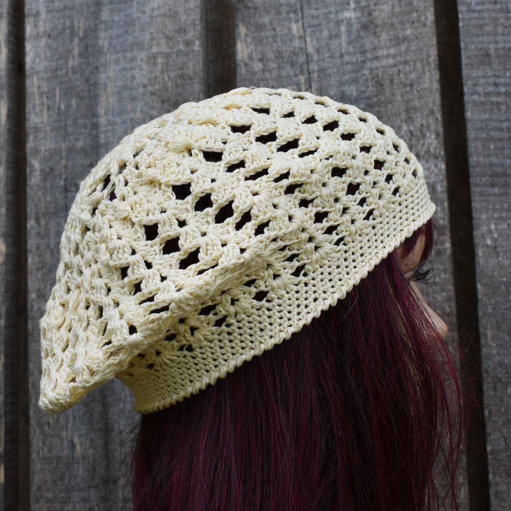 Crocheted beige hat worn by a person with dark hair against a wooden background