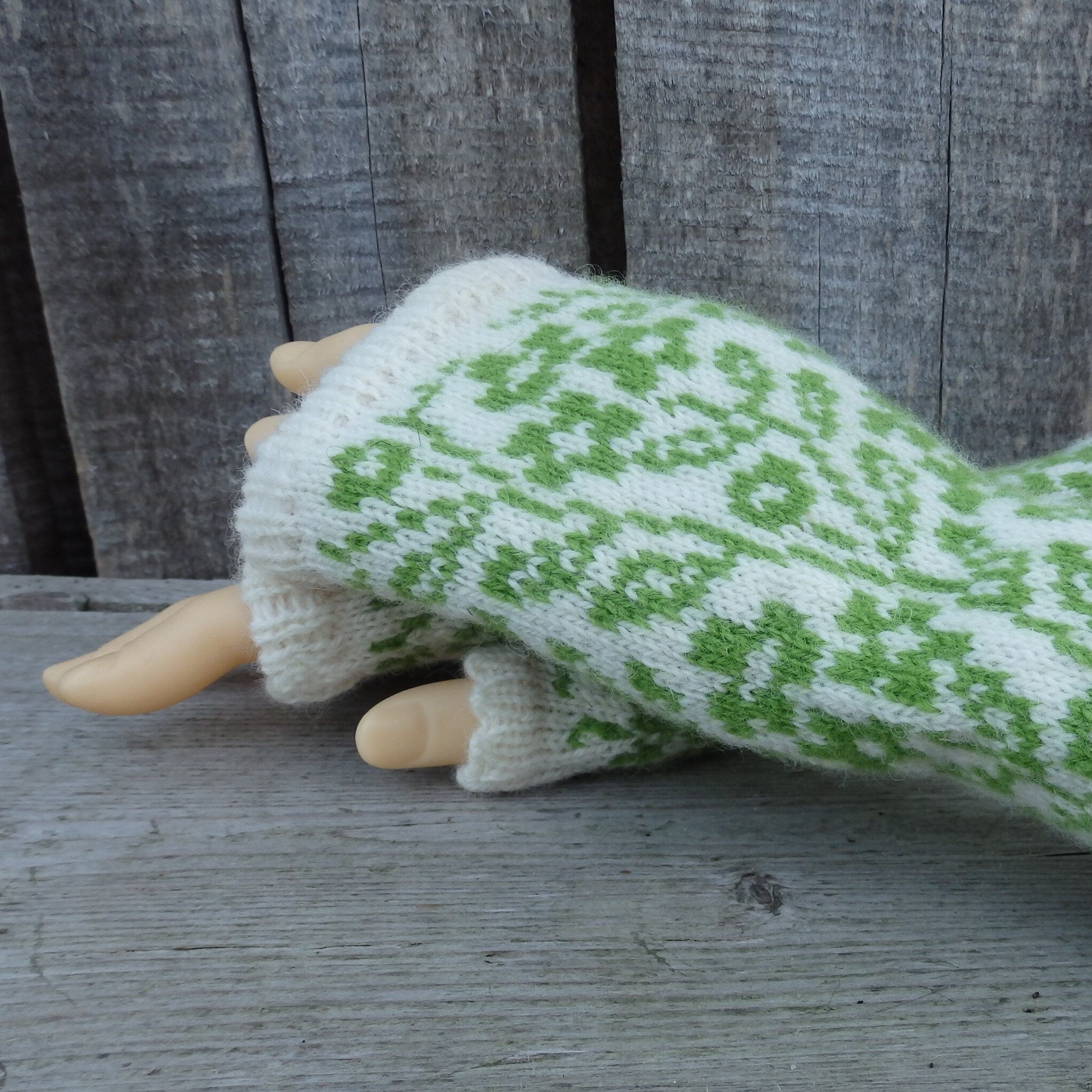 White and green patterned fingerless gloves on a mannequin arm against a wooden background