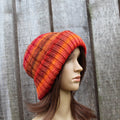 Mannequin head wearing a red and orange striped knit beanie against a wooden background